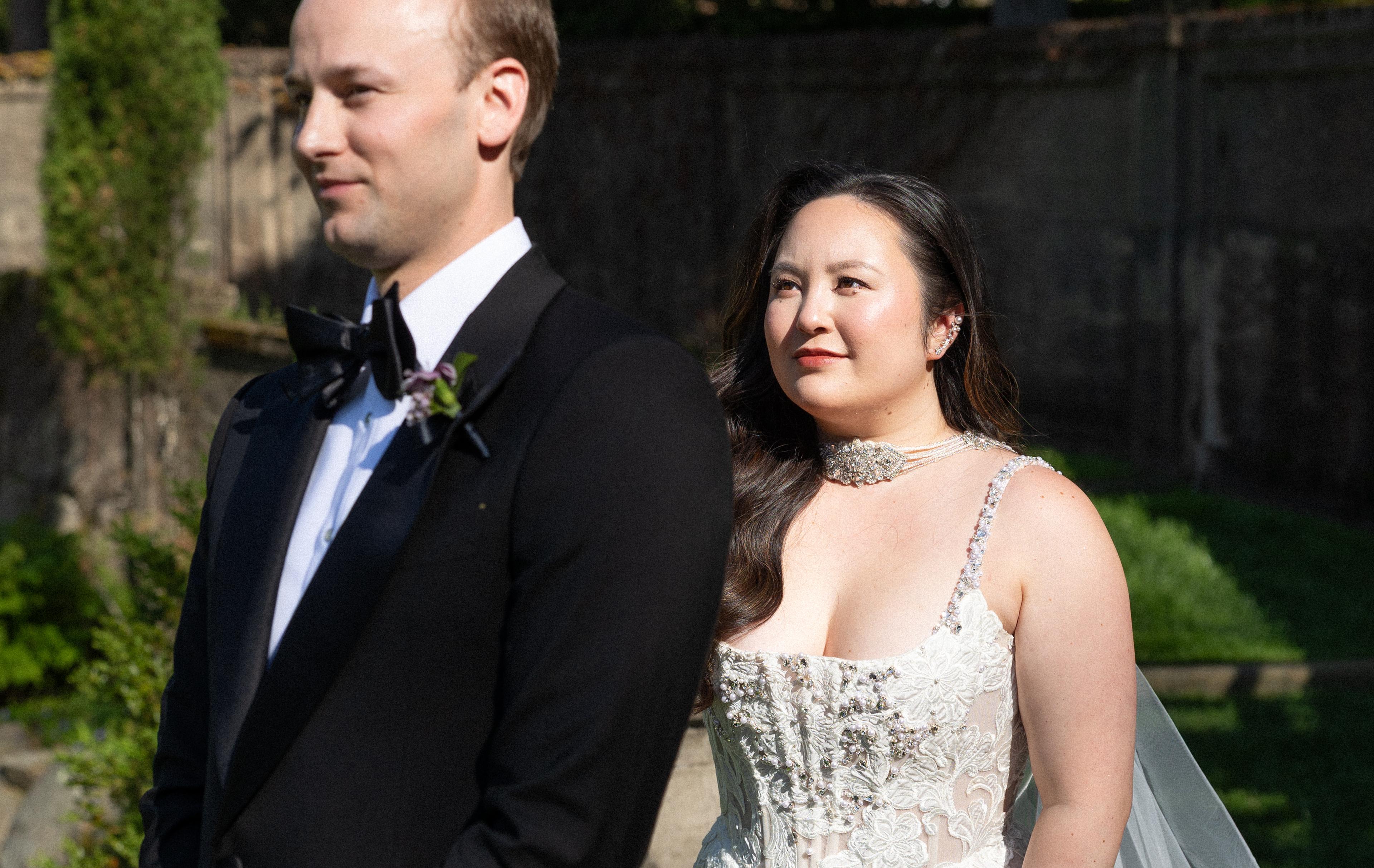 Groom stands in a tux as bride walks behind in a wedding dress