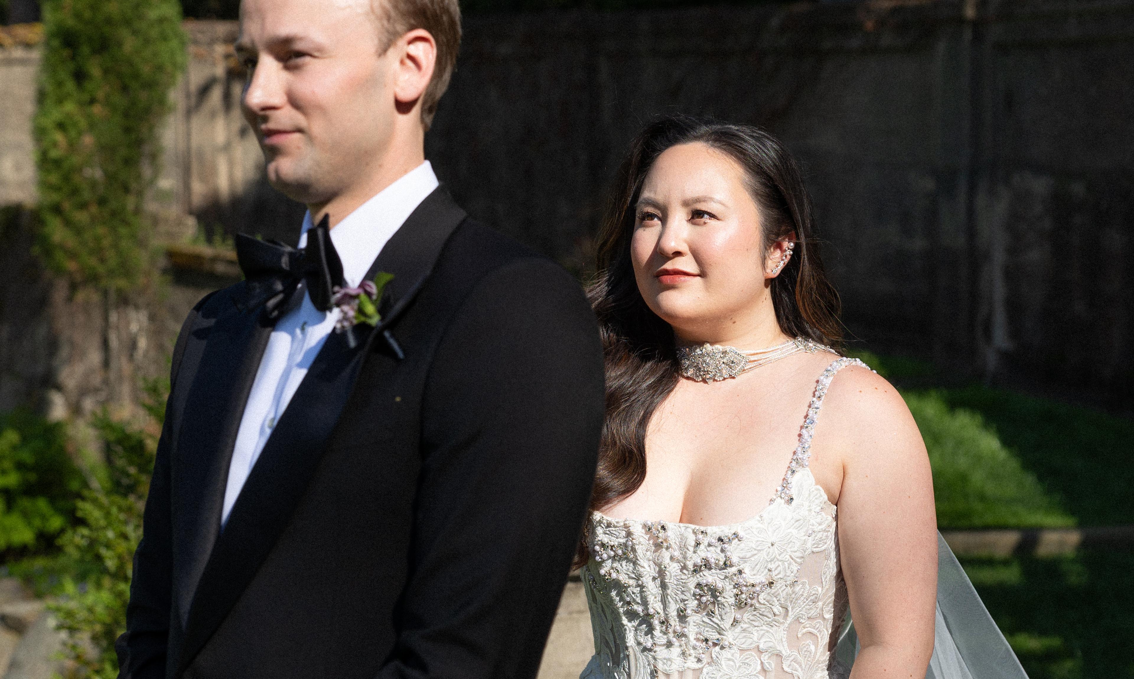 Groom stands in a tux as bride walks behind in a wedding dress