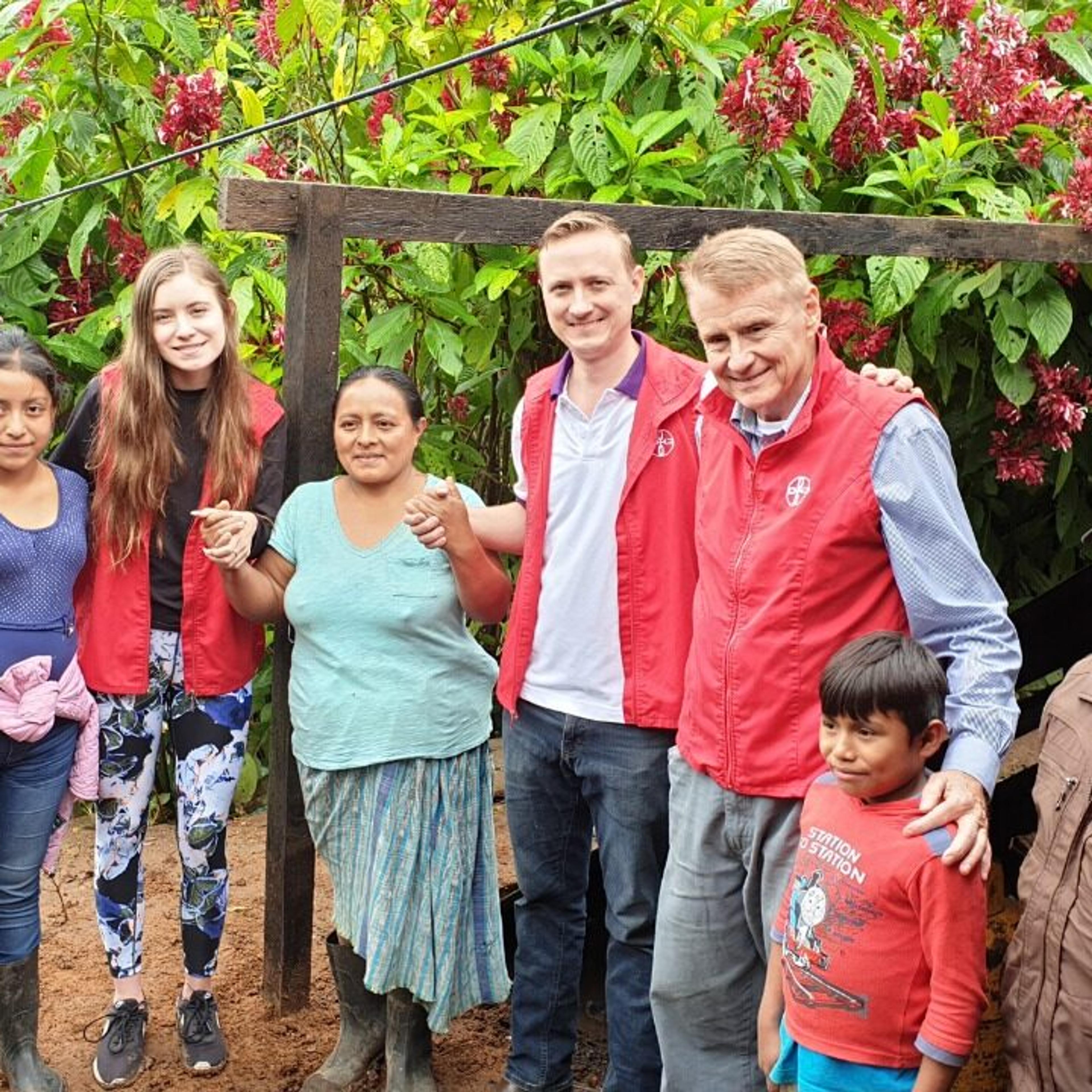 Group of men, women and children standing in front of greenery