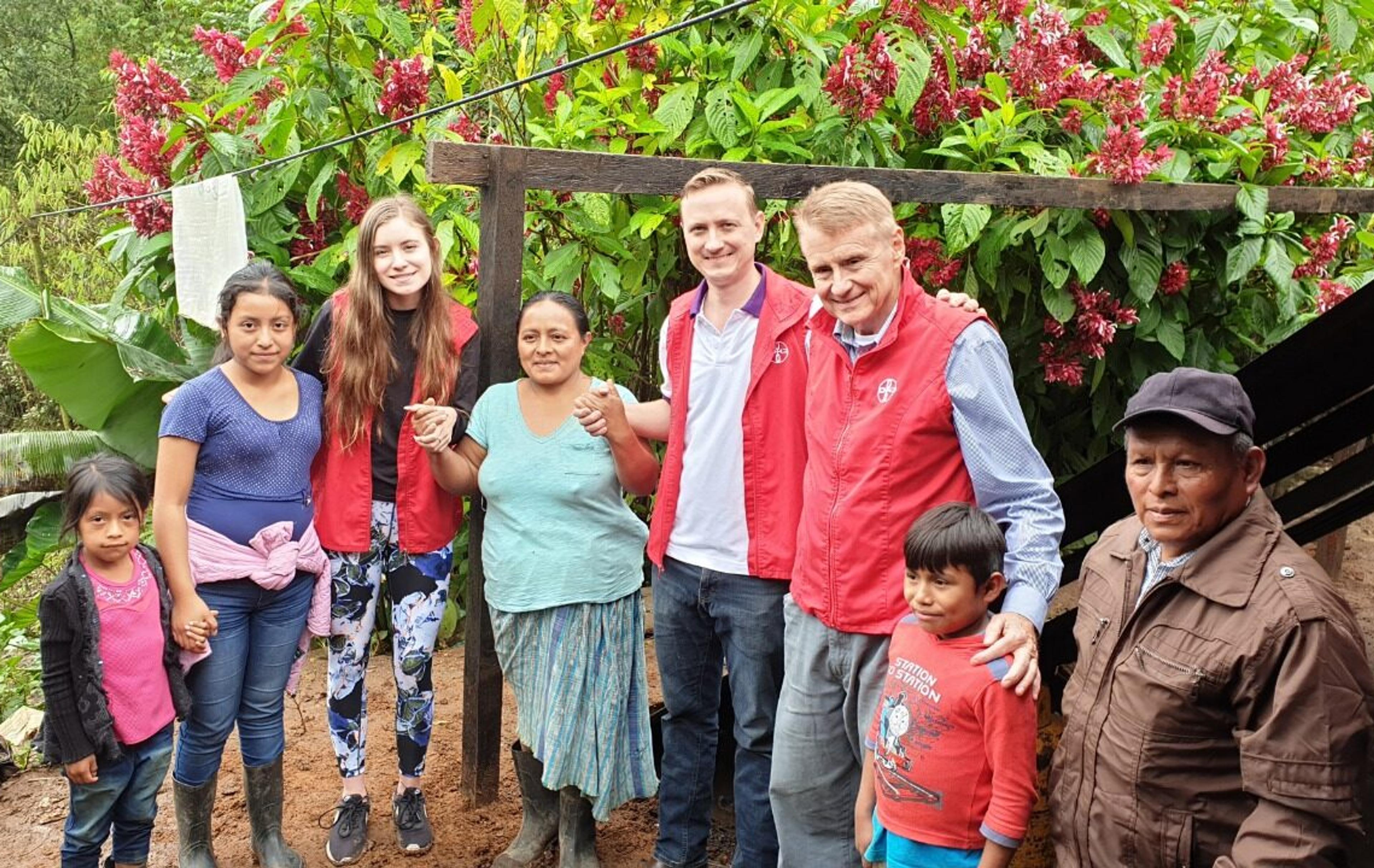 Group of men, women and children standing in front of greenery