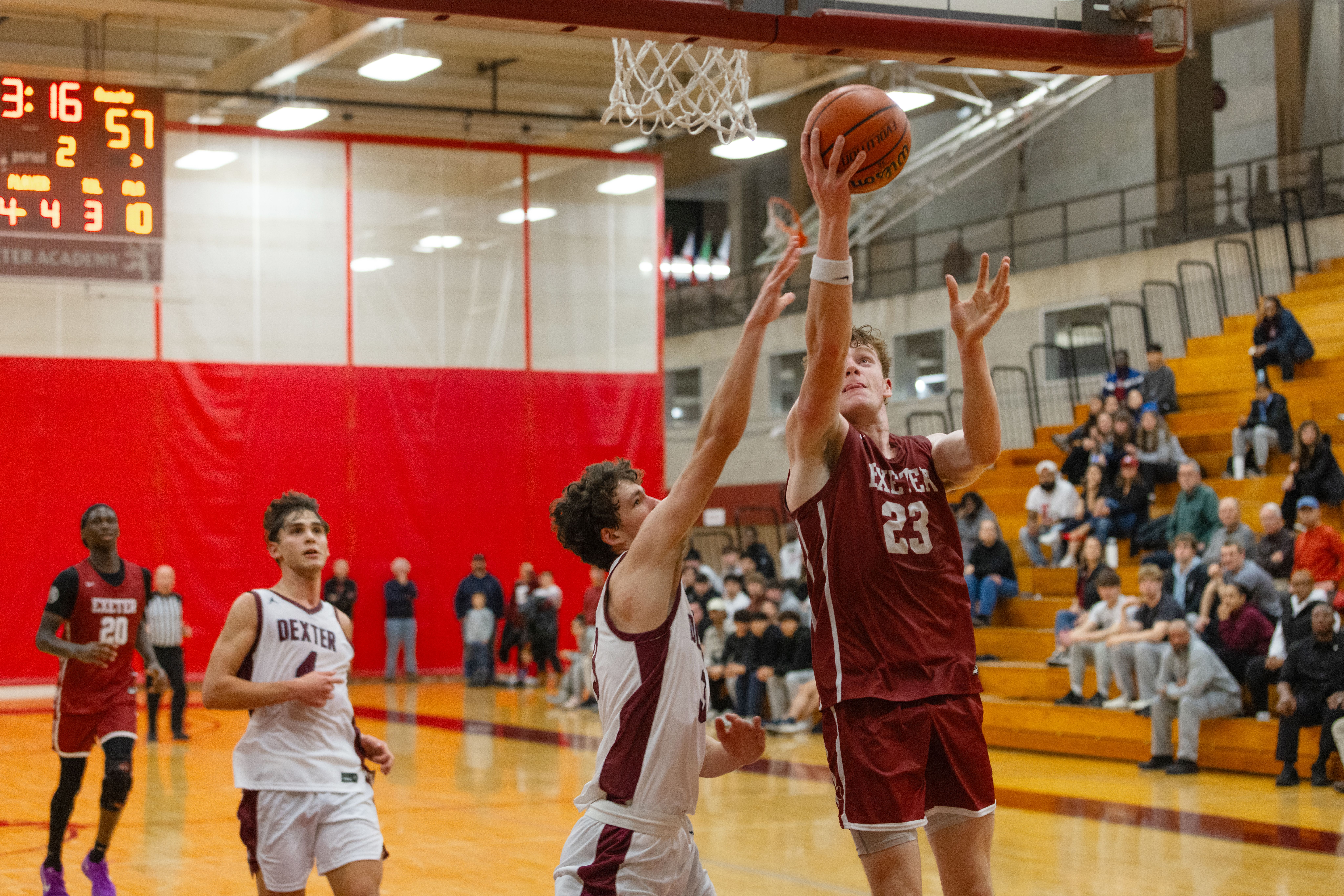 Four boys on a basketball court as one goes for a lay up into the basket