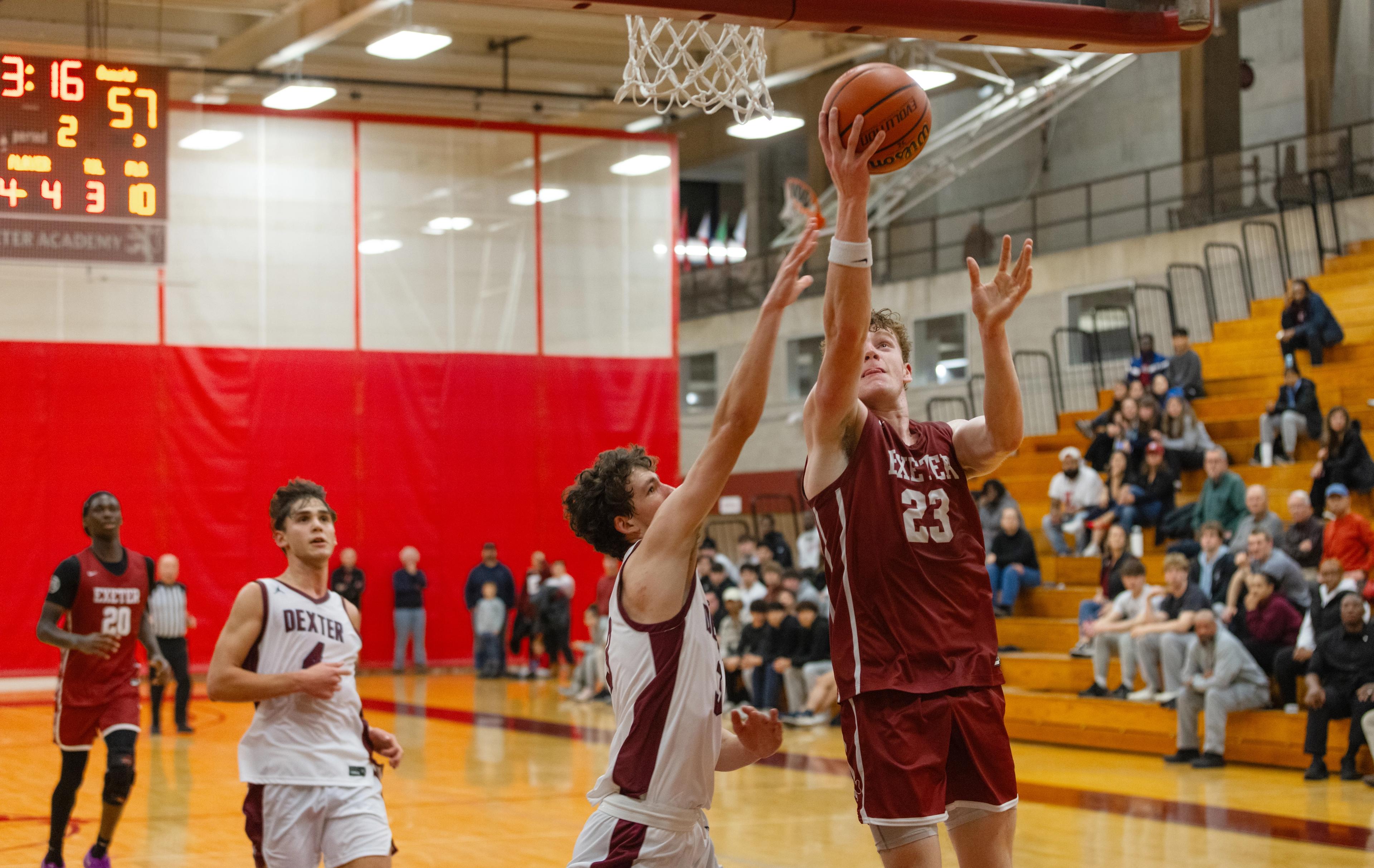Four boys on a basketball court as one goes for a lay up into the basket