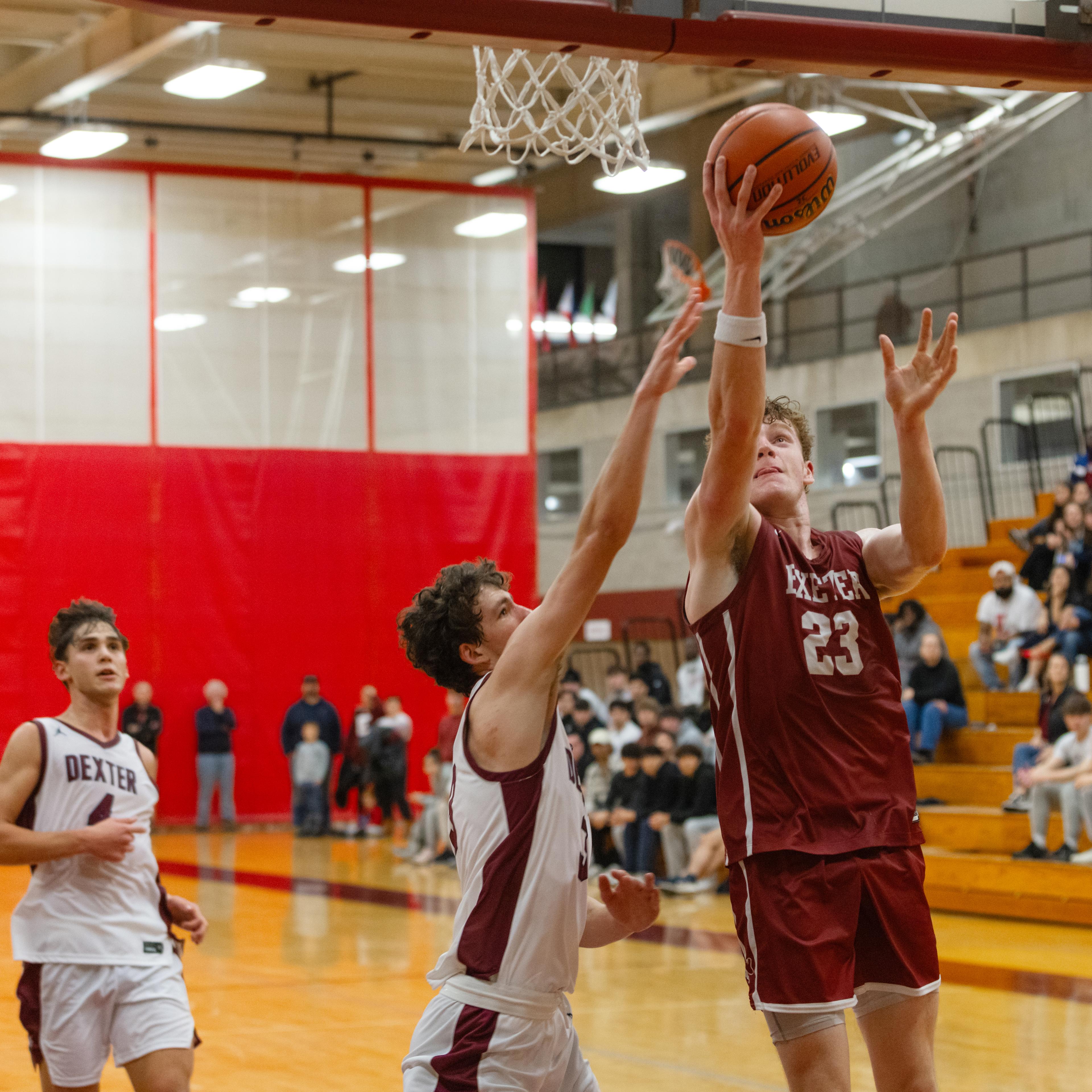Four boys on a basketball court as one goes for a lay up into the basket