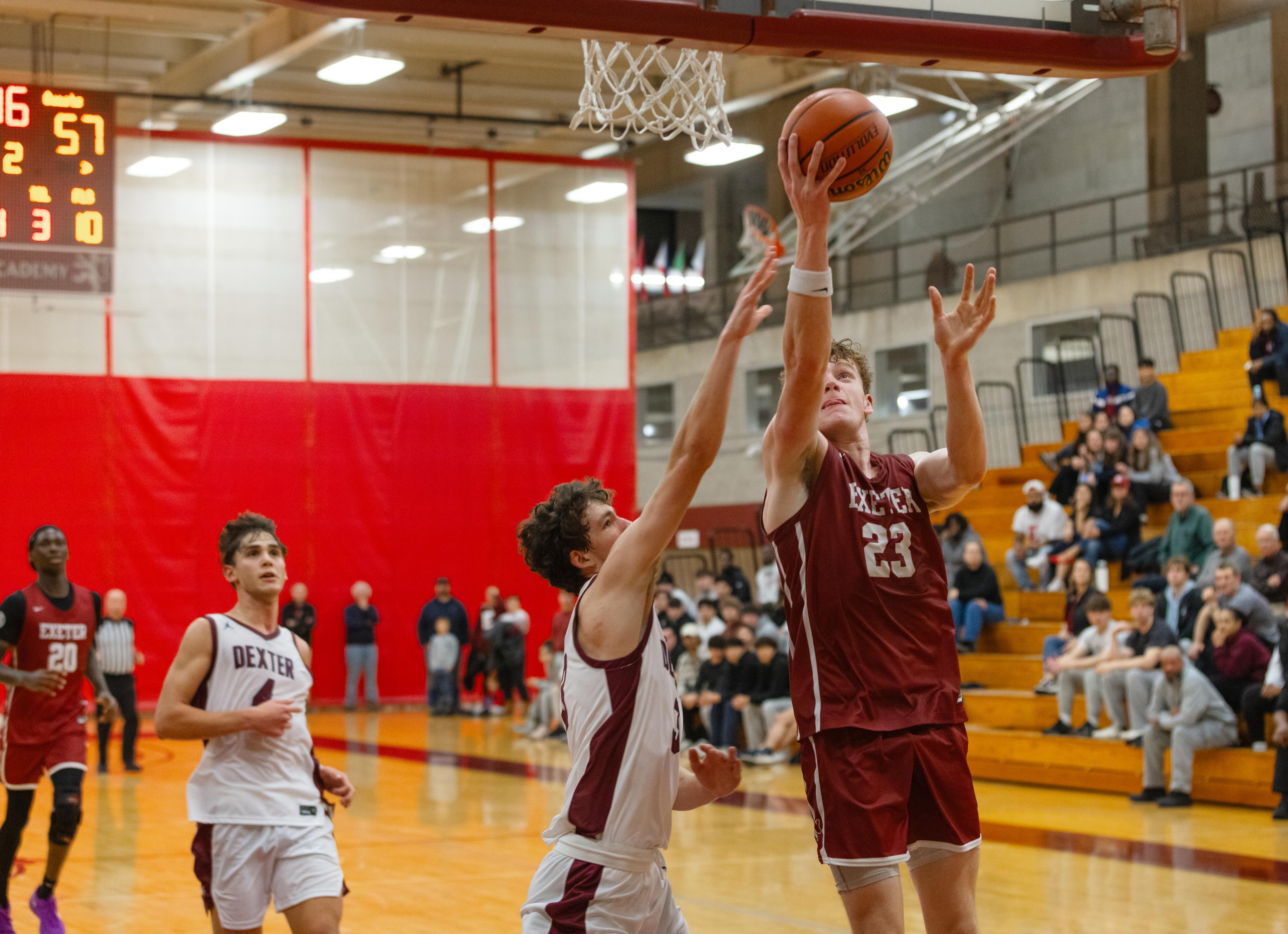 Four boys on a basketball court as one goes for a lay up into the basket