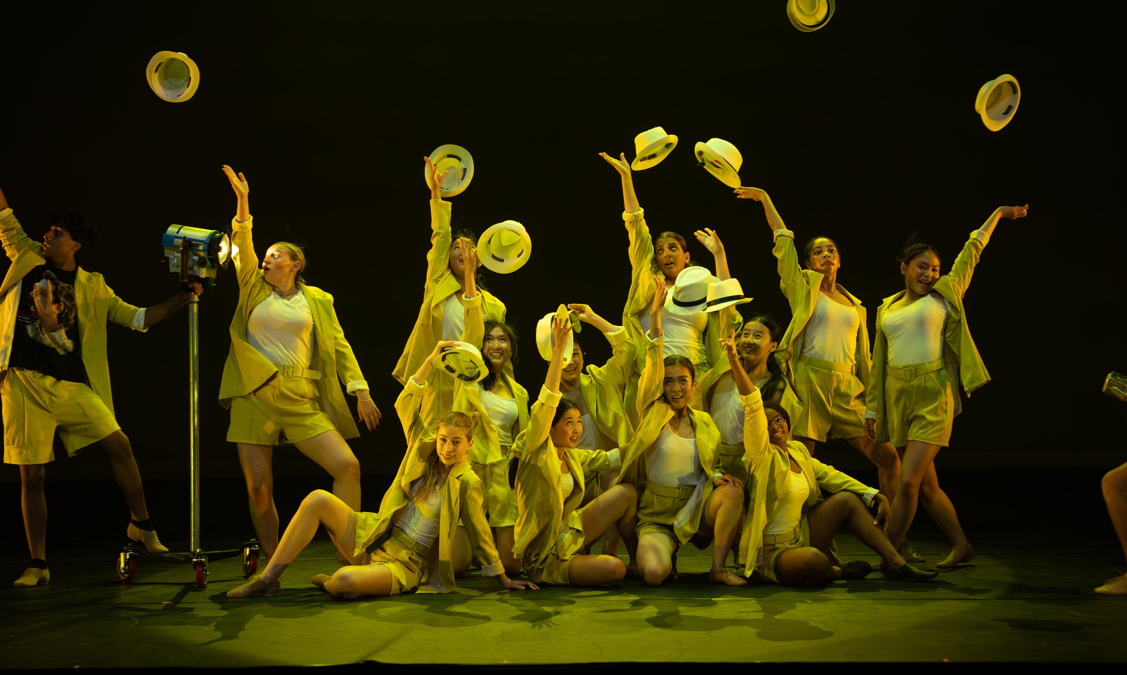 Large group of dancers in suits on pose and throw hats on stage