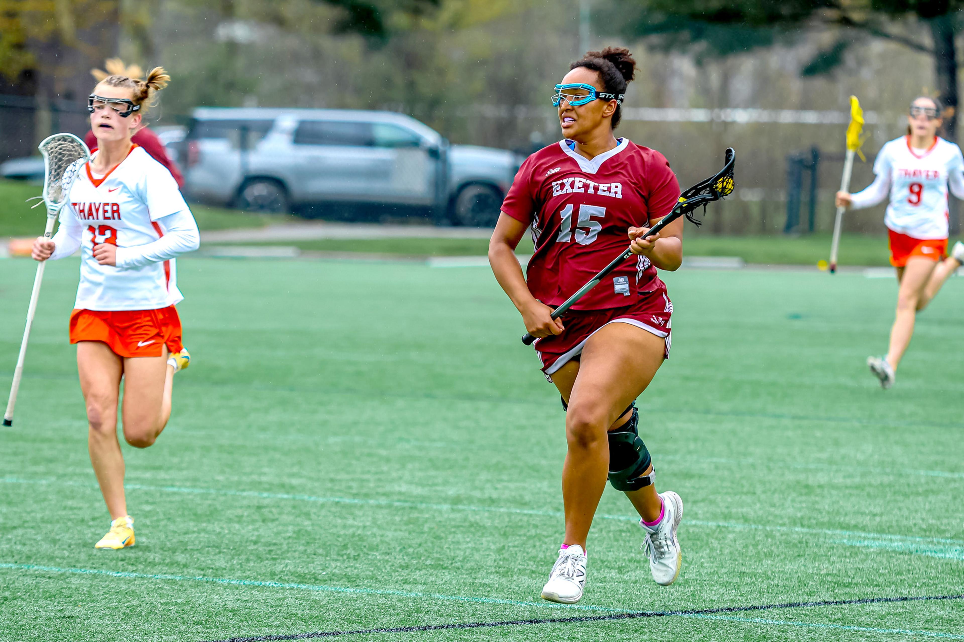 Girl runs across field with lacrosse stick