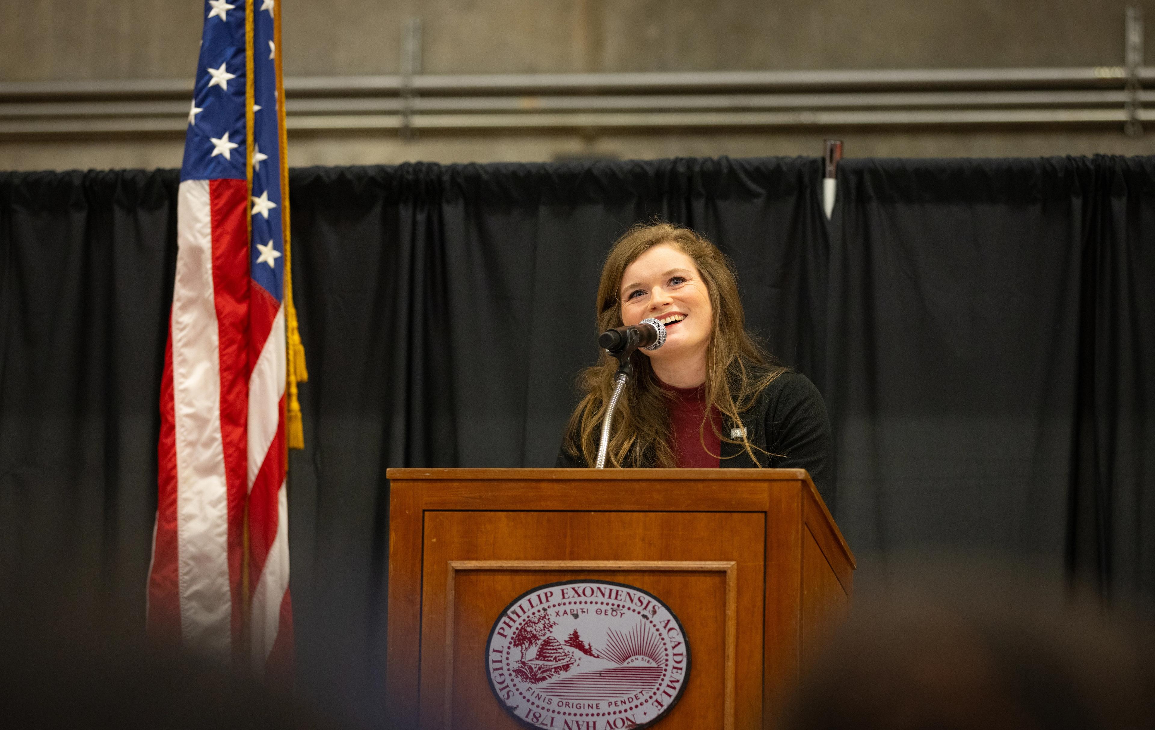 woman standing at lectern with flag