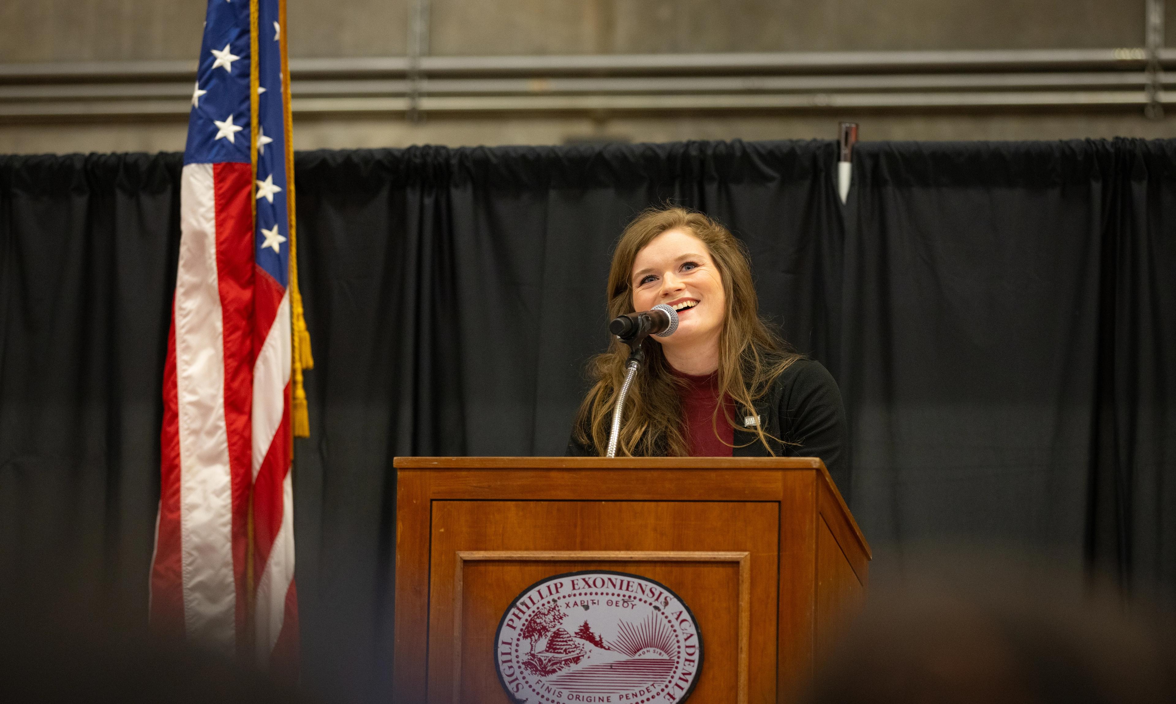 woman standing at lectern with flag