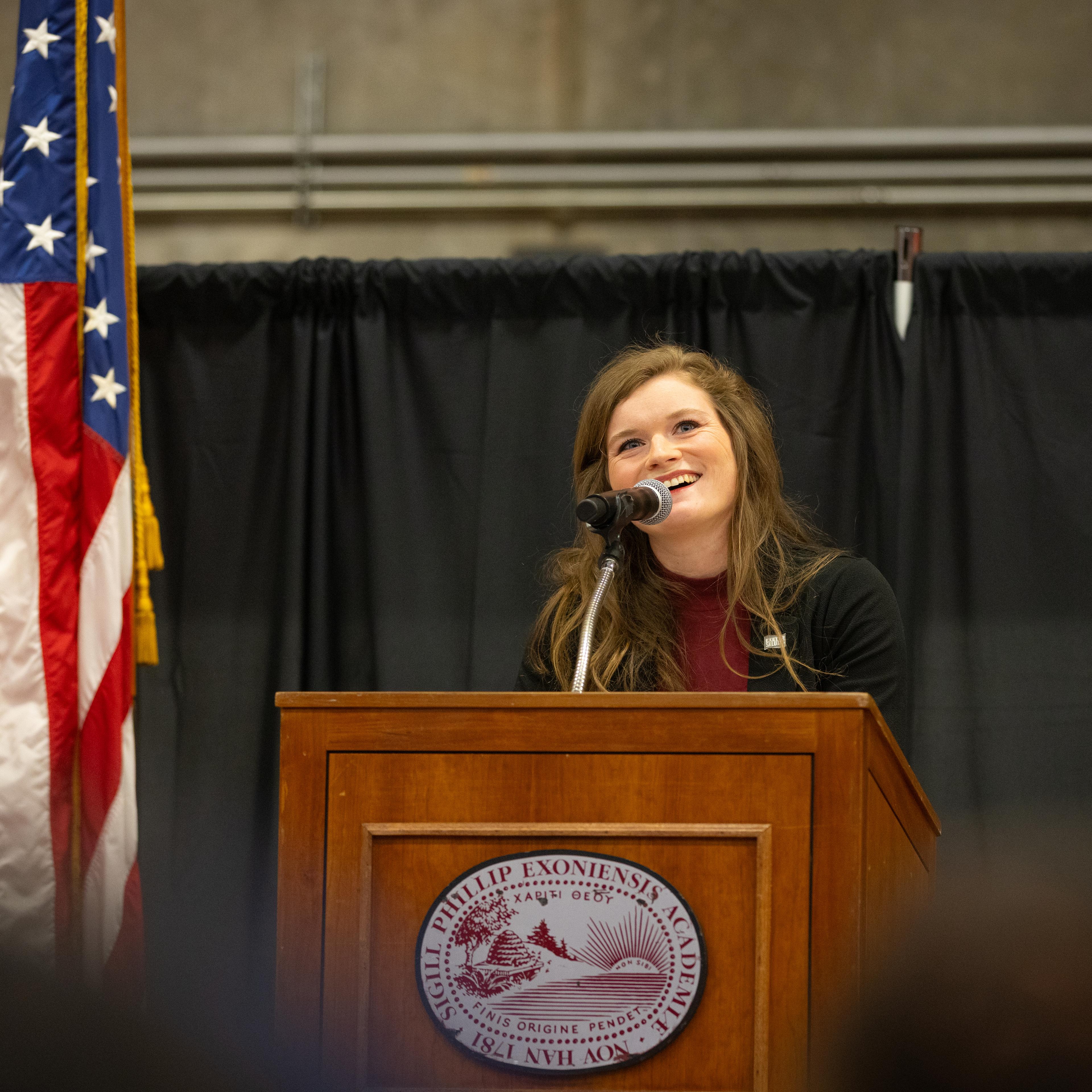 woman standing at lectern with flag