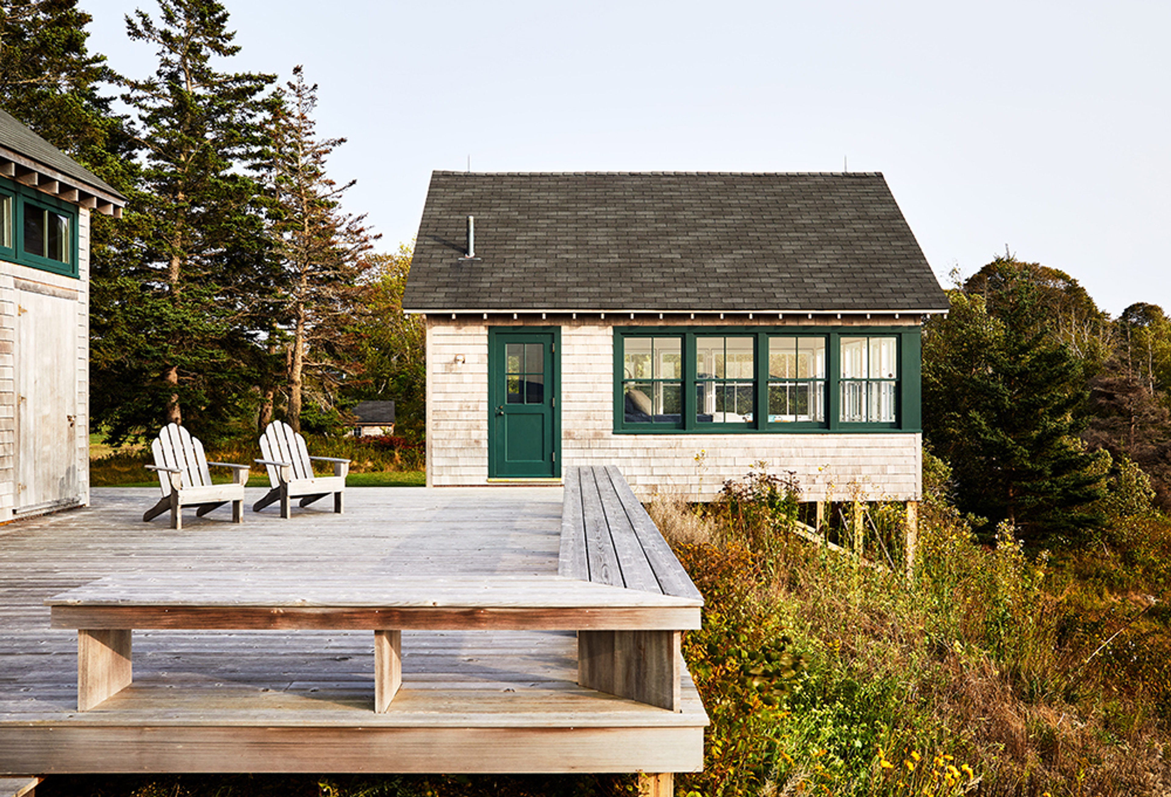 White cottage with green shutters sits on grassy hill