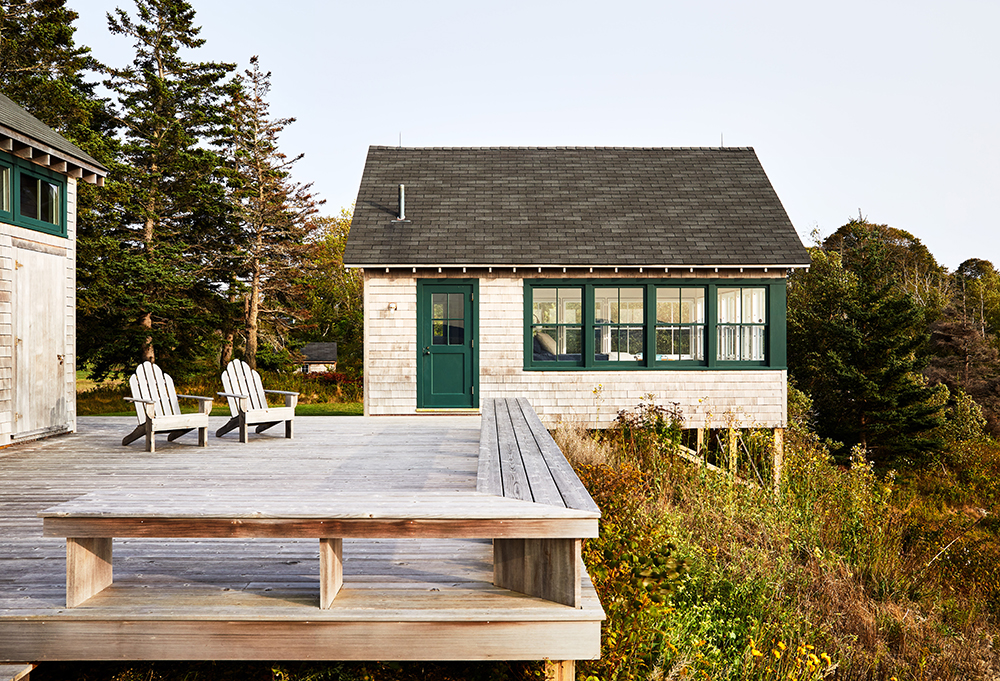 White cottage with green shutters sits on grassy hill