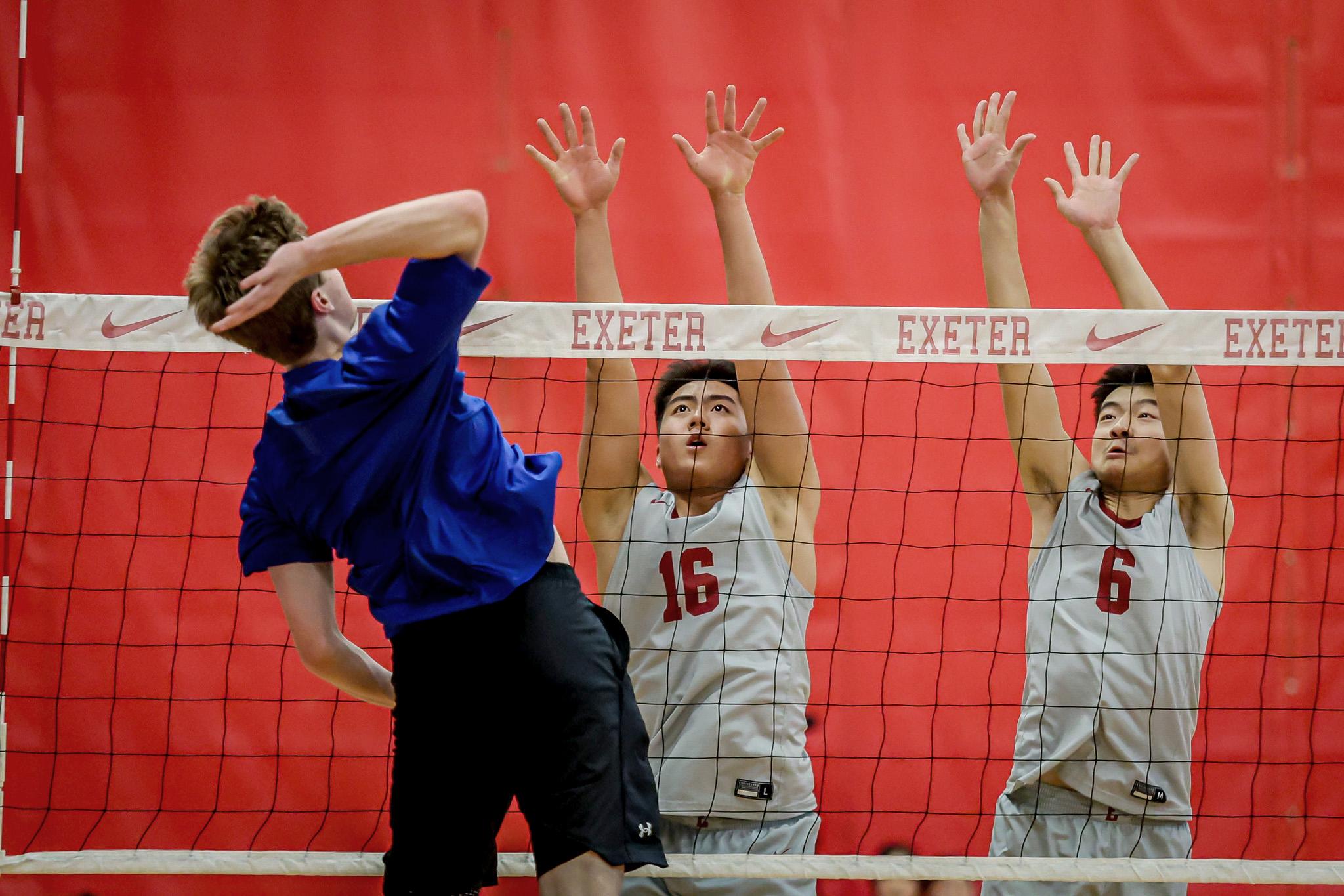 Three boys jump at volleyball net