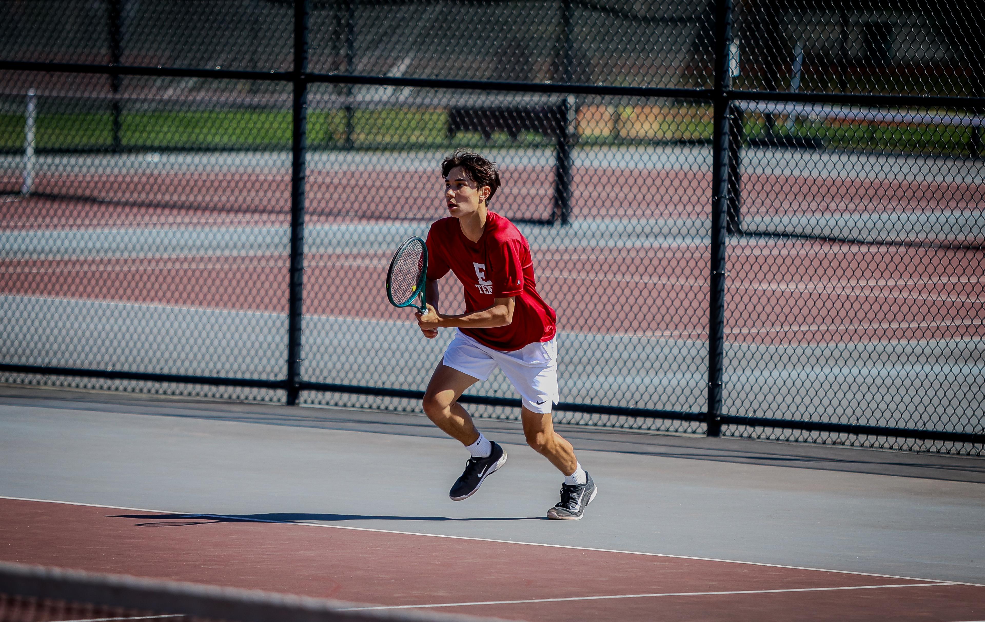 Boy runs towards tennis ball while holding a racket