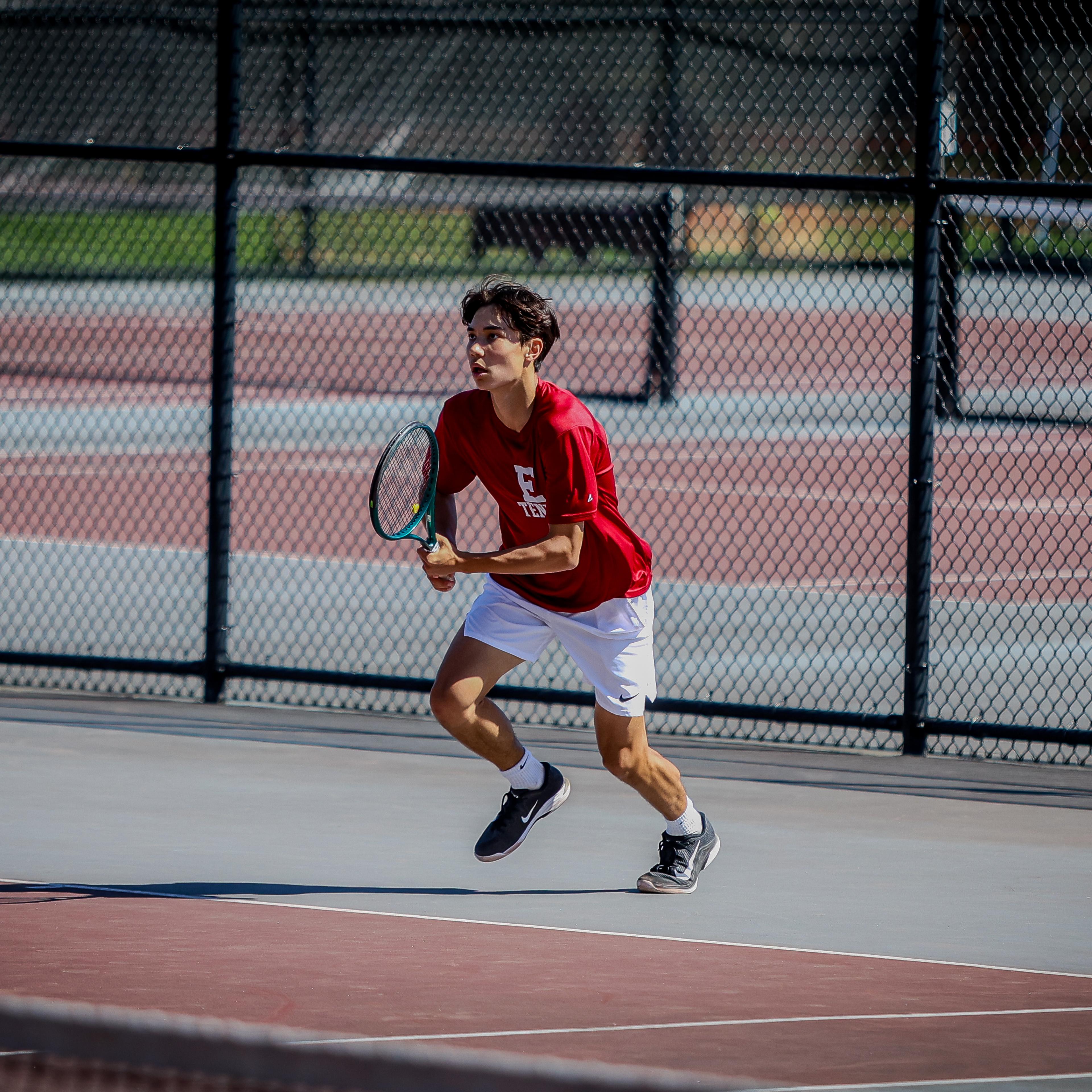 Boy runs towards tennis ball while holding a racket