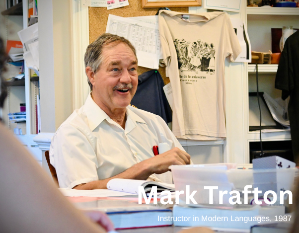 A teacher sits at a table and smiles.