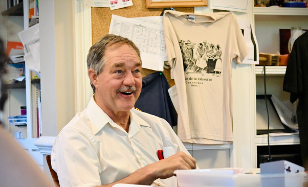 A teacher sits at a table and smiles.