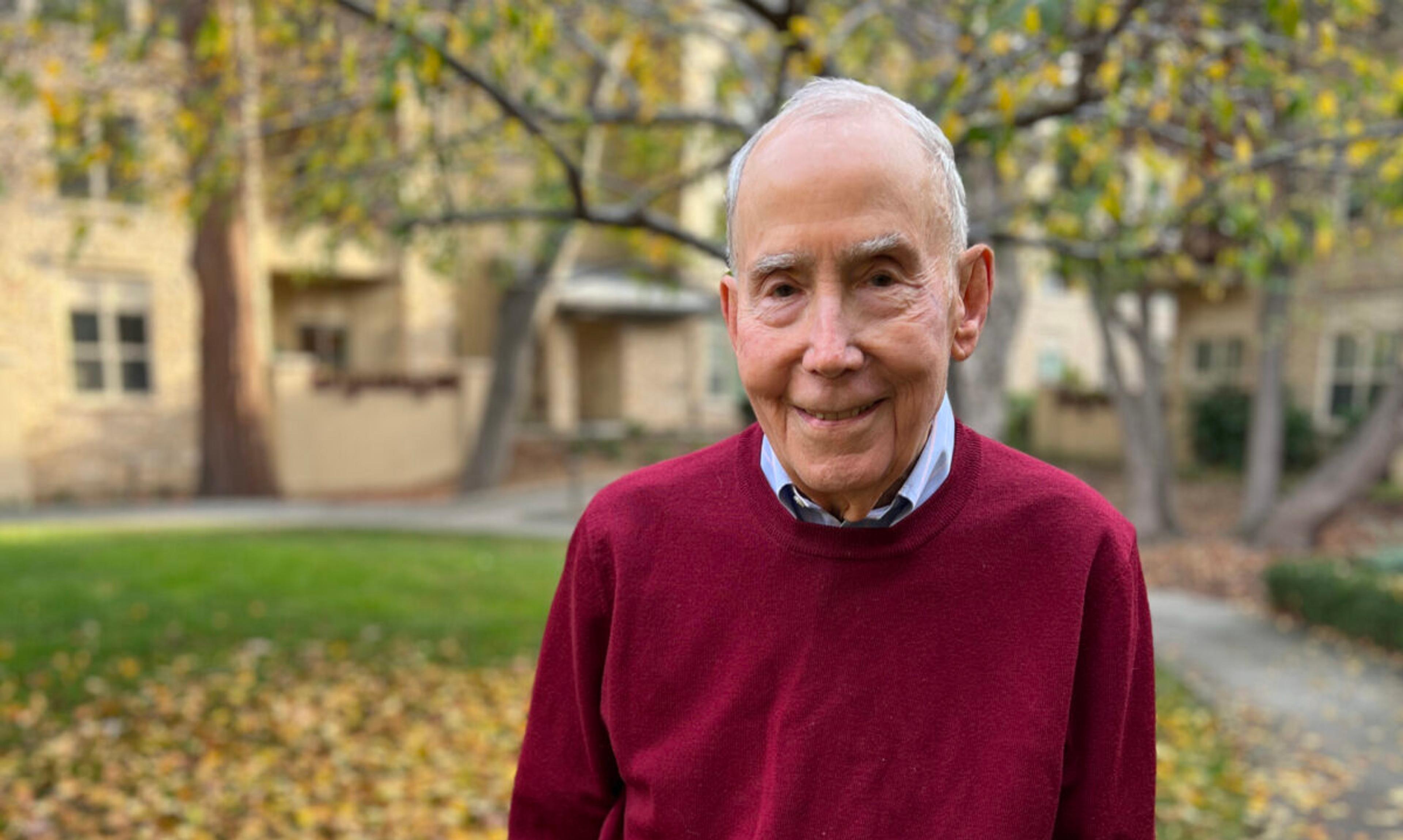 Elderly man stands on lawn covered in leaves