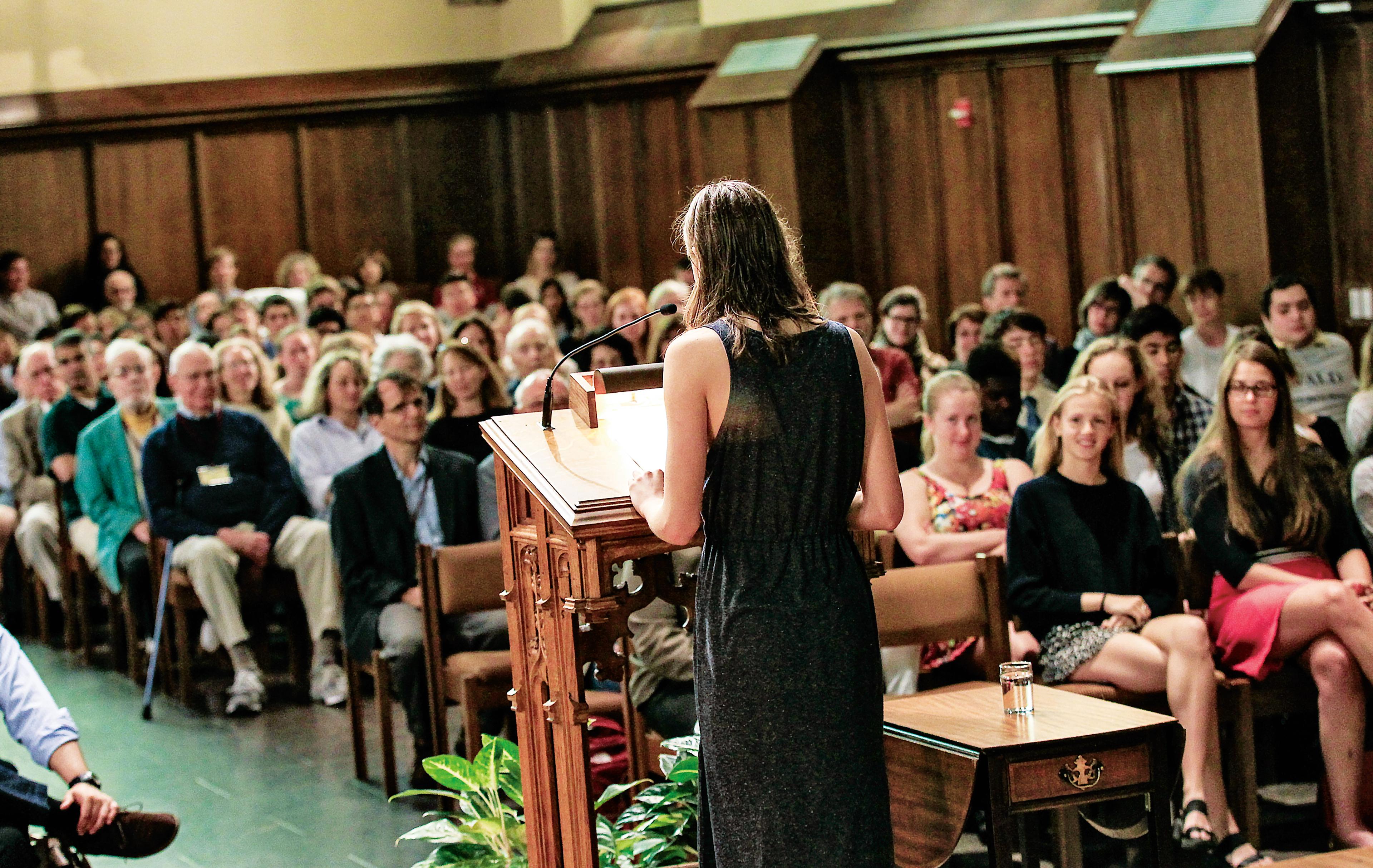 Woman stands at podium in front of a crowd in church pews