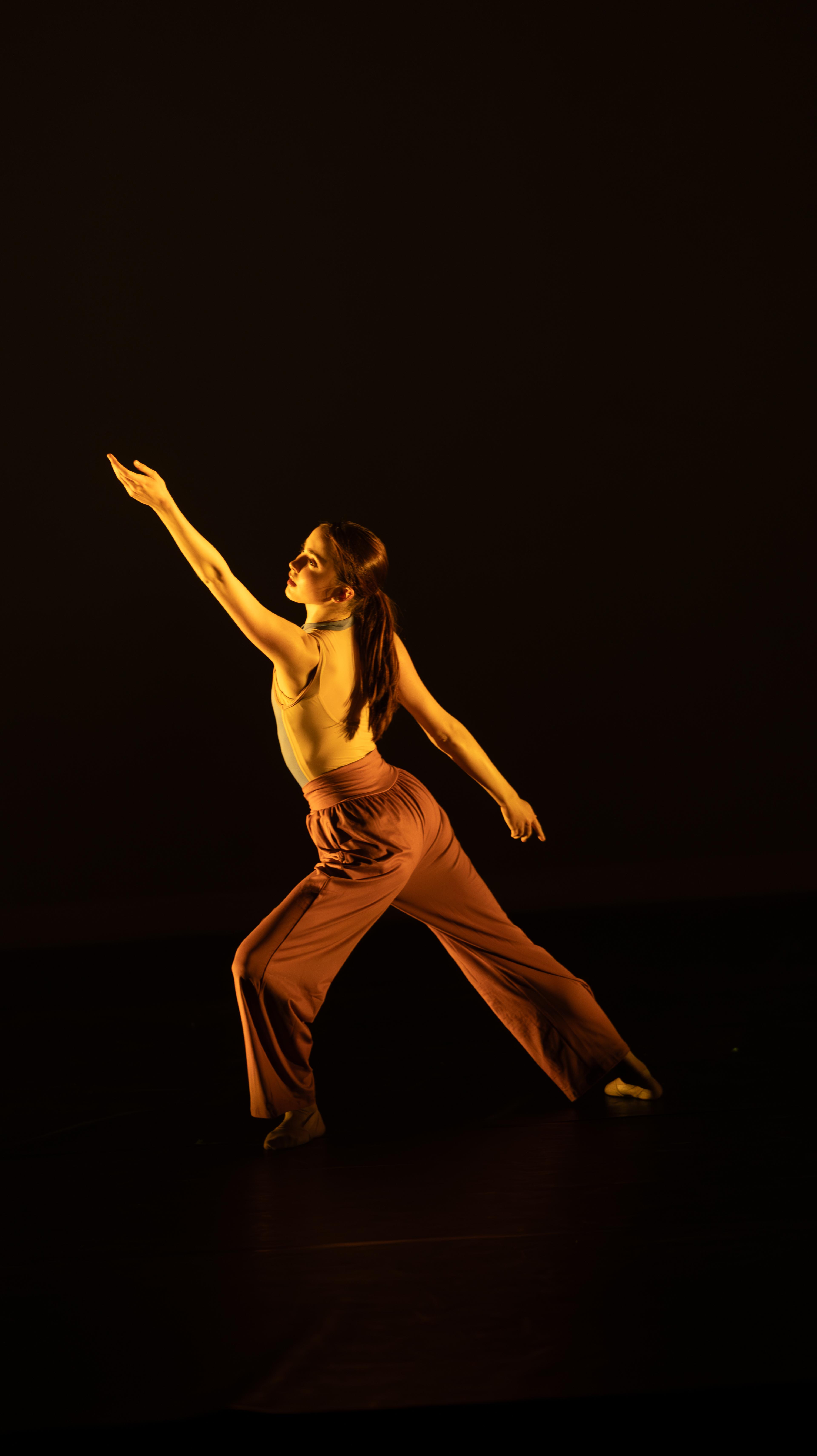 Dancer poses on stage under orange light