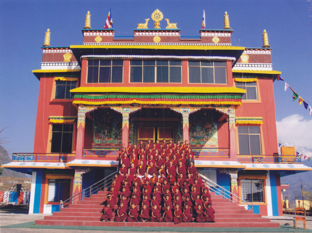 Monks line up outside of a red and yellow Buddhist monastery
