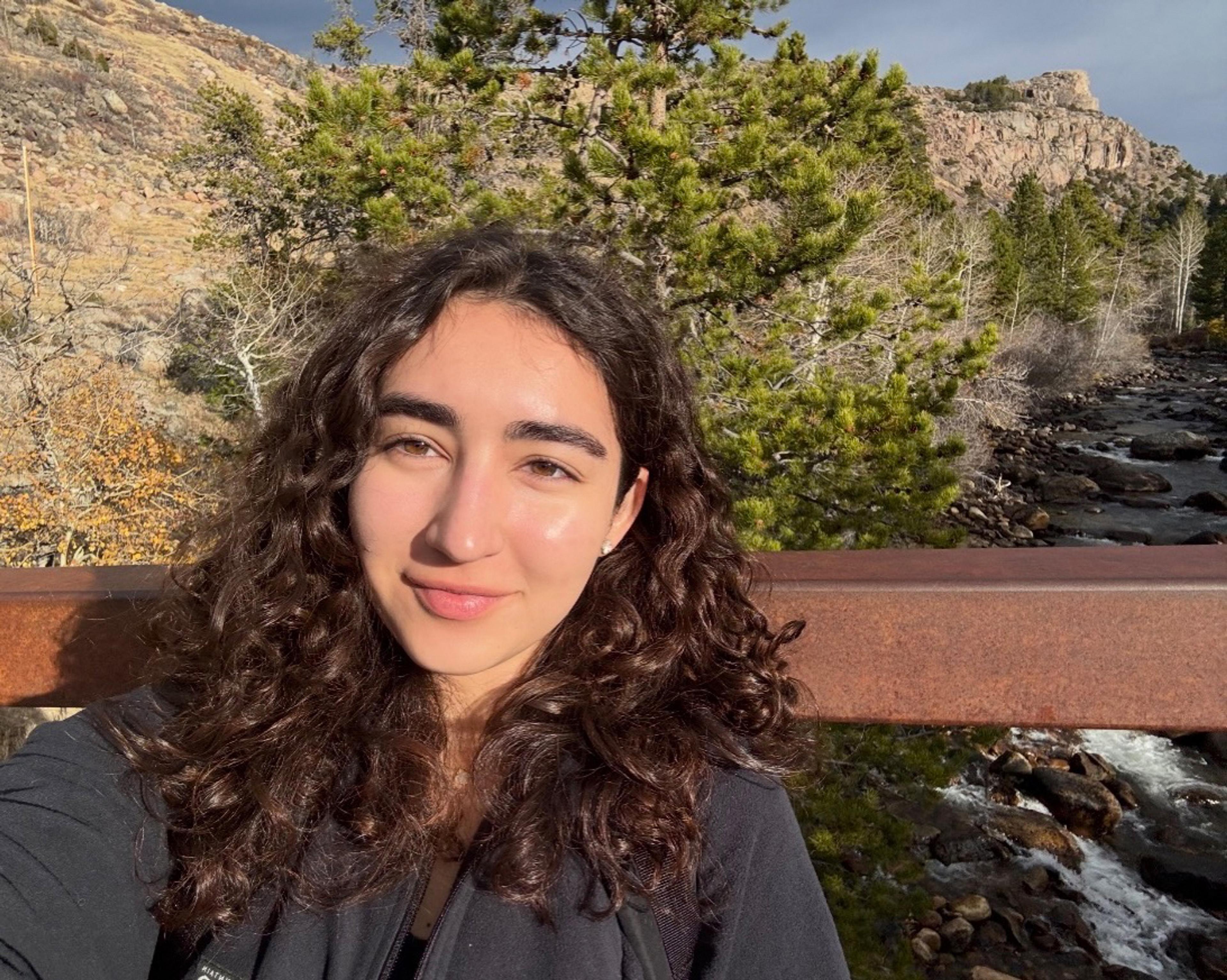 girl with curly brown hair in front of a river