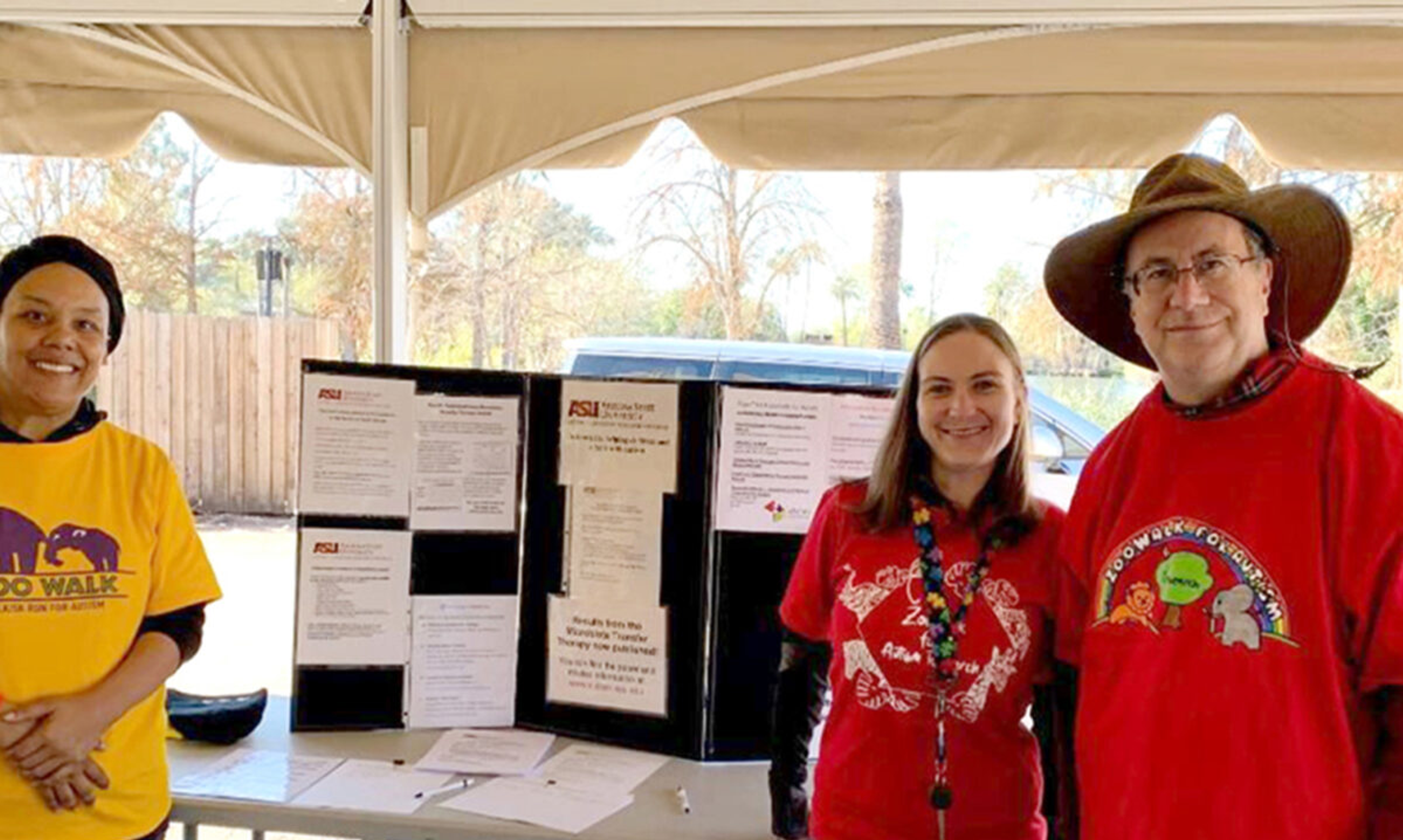 Three people stand in front of a table with a trifold poster board