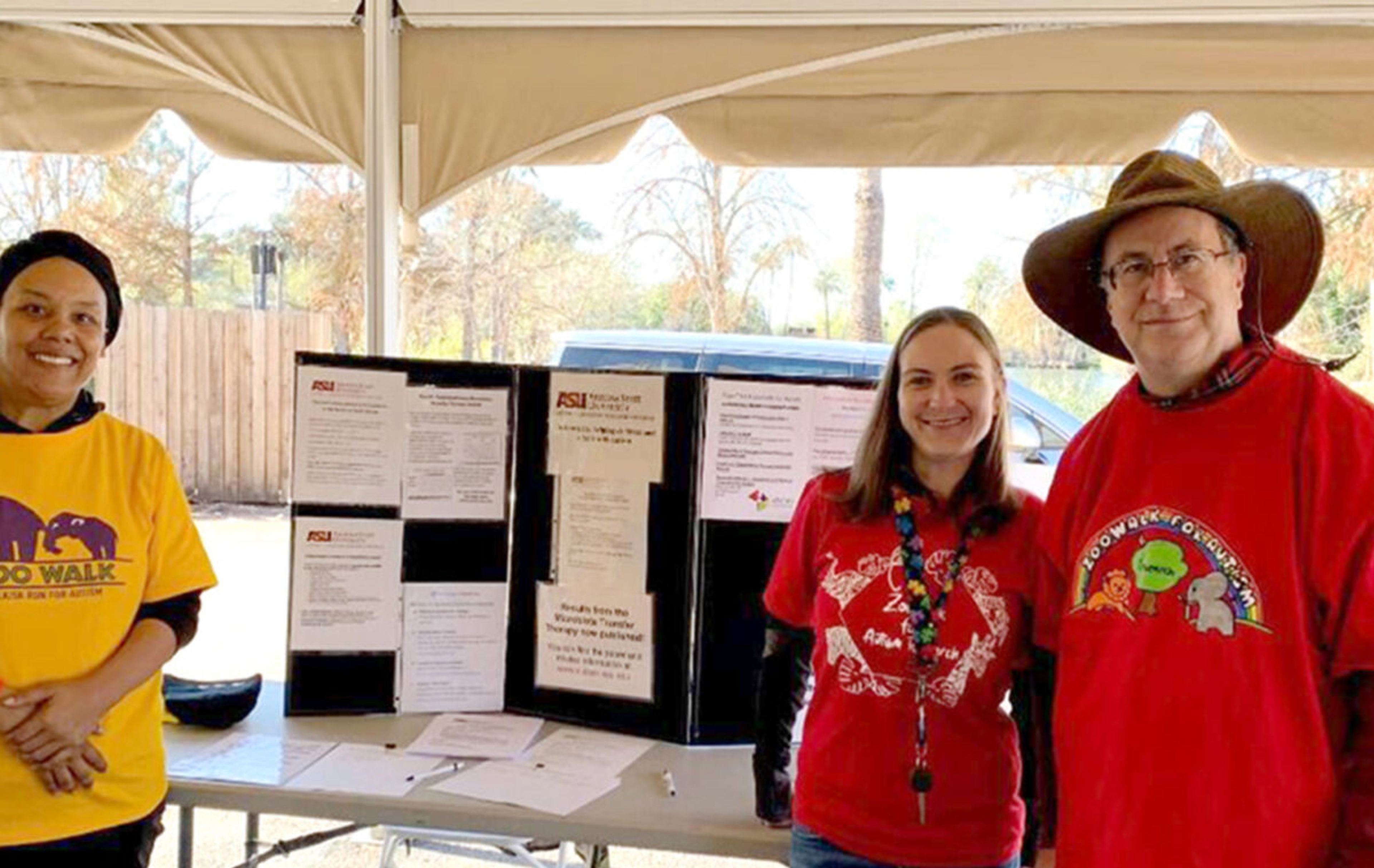 Three people stand in front of a table with a trifold poster board