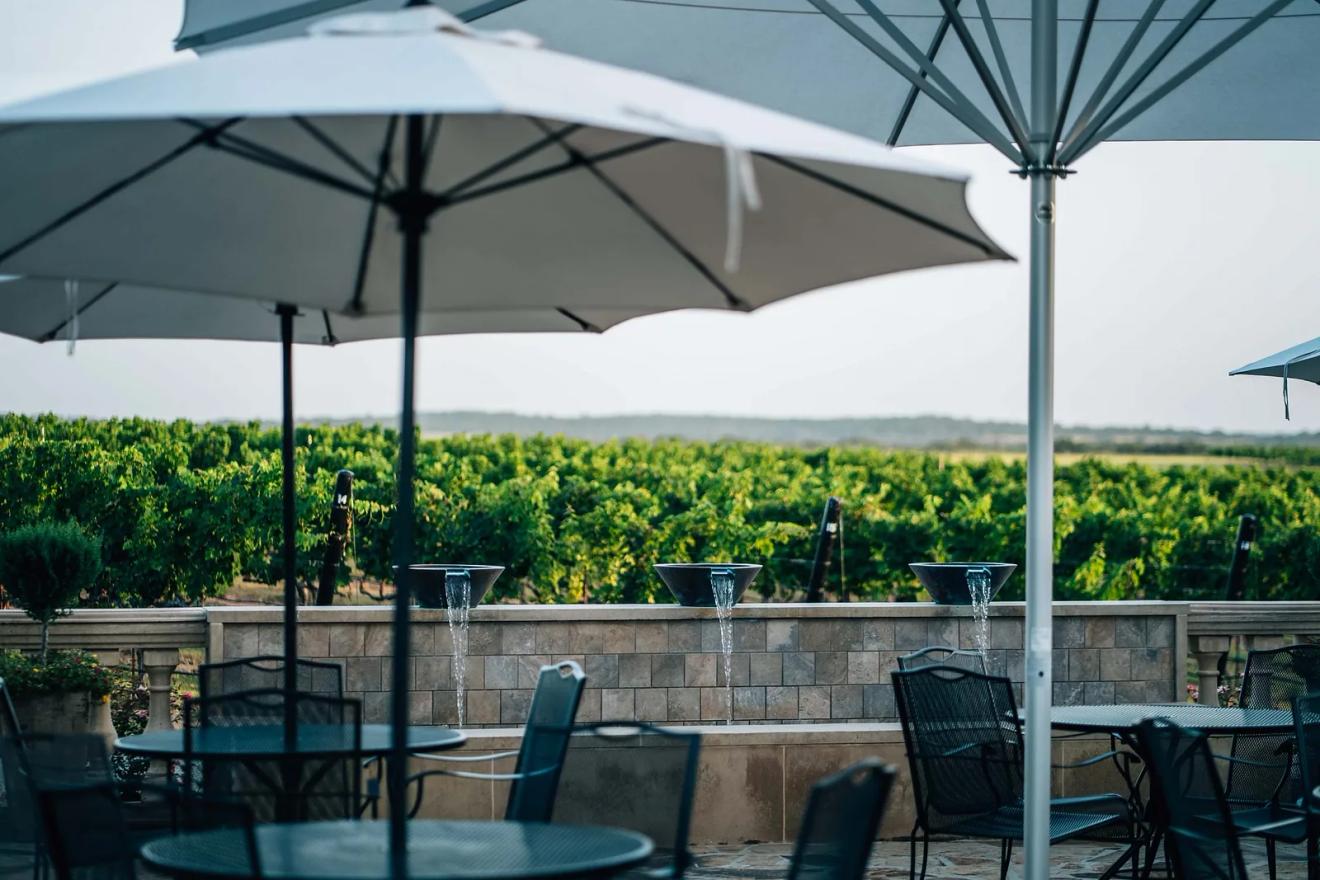 Umbrella-shaded patio tables looking out over the vines at Grape Creek Vineyards on the Fredericksburg wine road