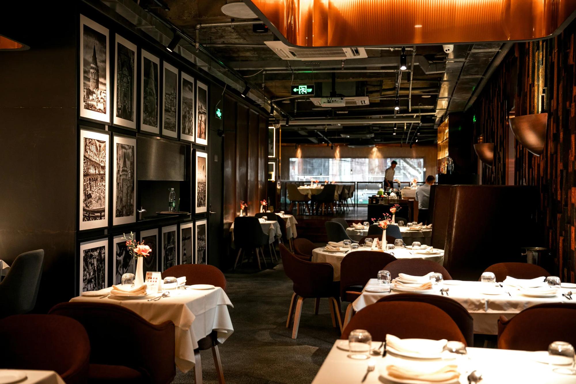 Upscale restaurant interior with set tables, leather chairs, and framed black-and-white photography wall