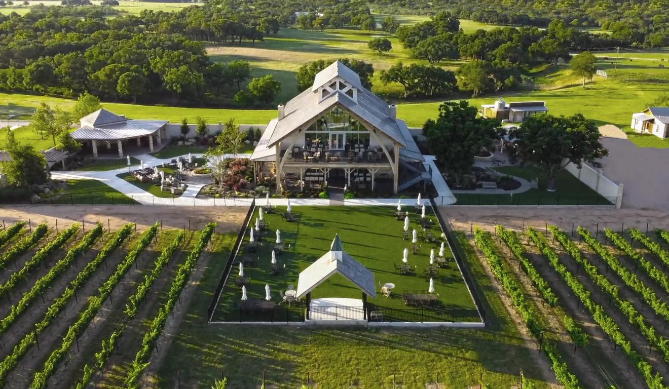 Aerial view of the timber-frame tasting room and vineyard rows at Augusta Vin winery in Fredericksburg, Texas