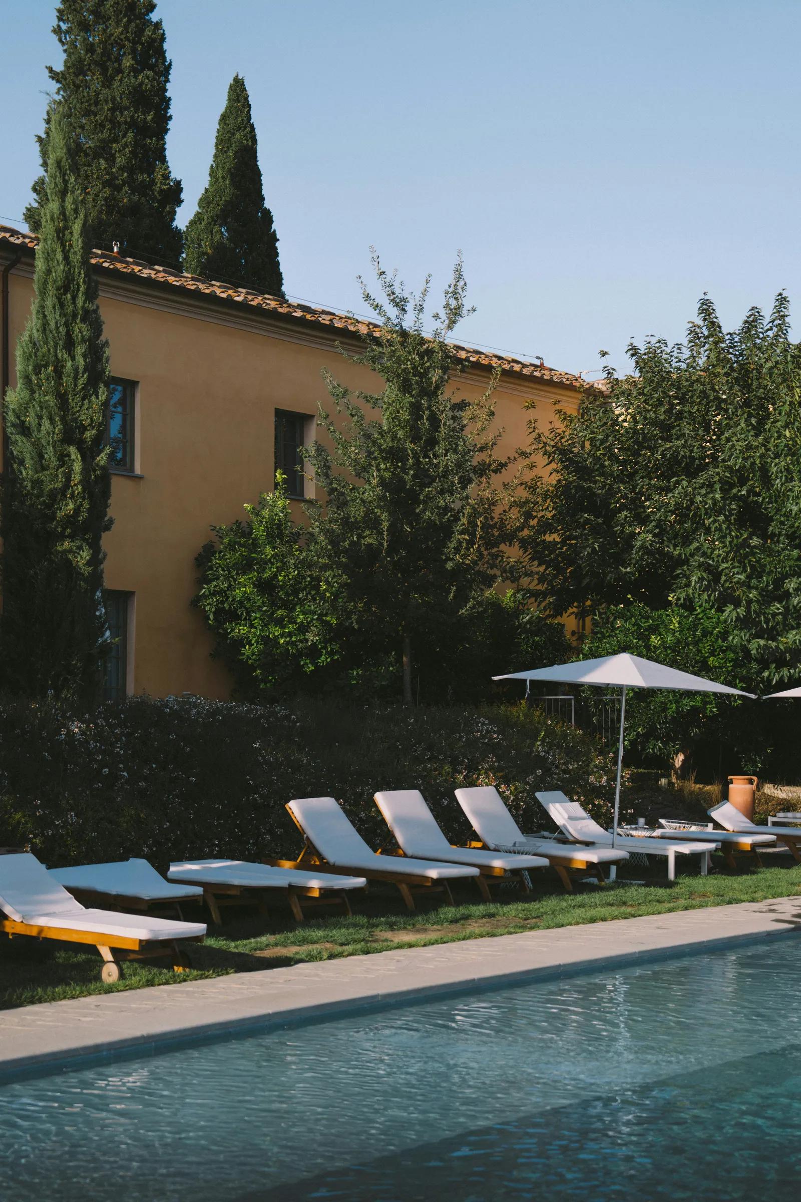 Poolside lounge chairs at a Tuscan villa vacation rental, surrounded by cypress trees and gardens
