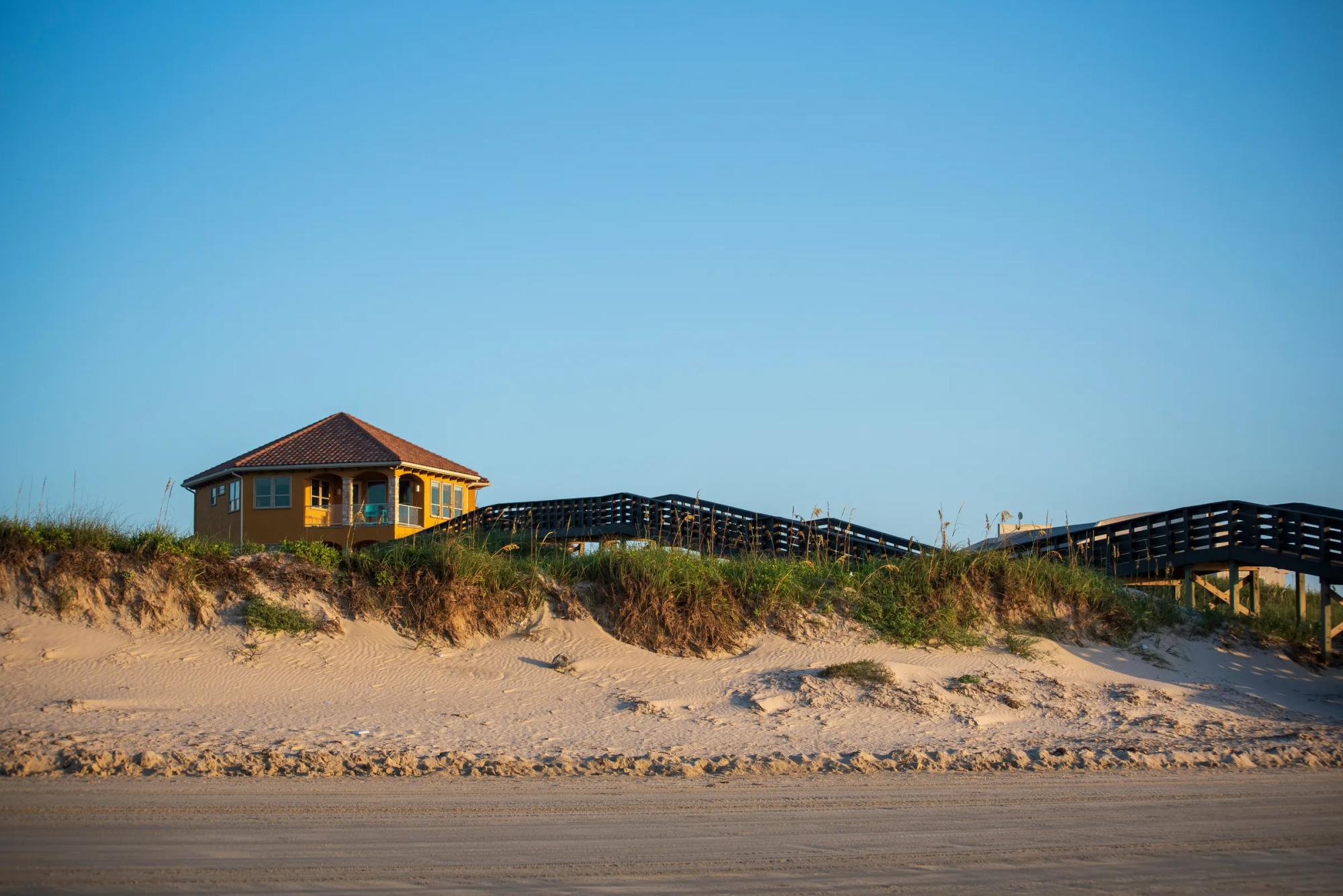 Yellow beach house on a dune with wooden boardwalk to the sandy beach, Airbnb rental exterior
