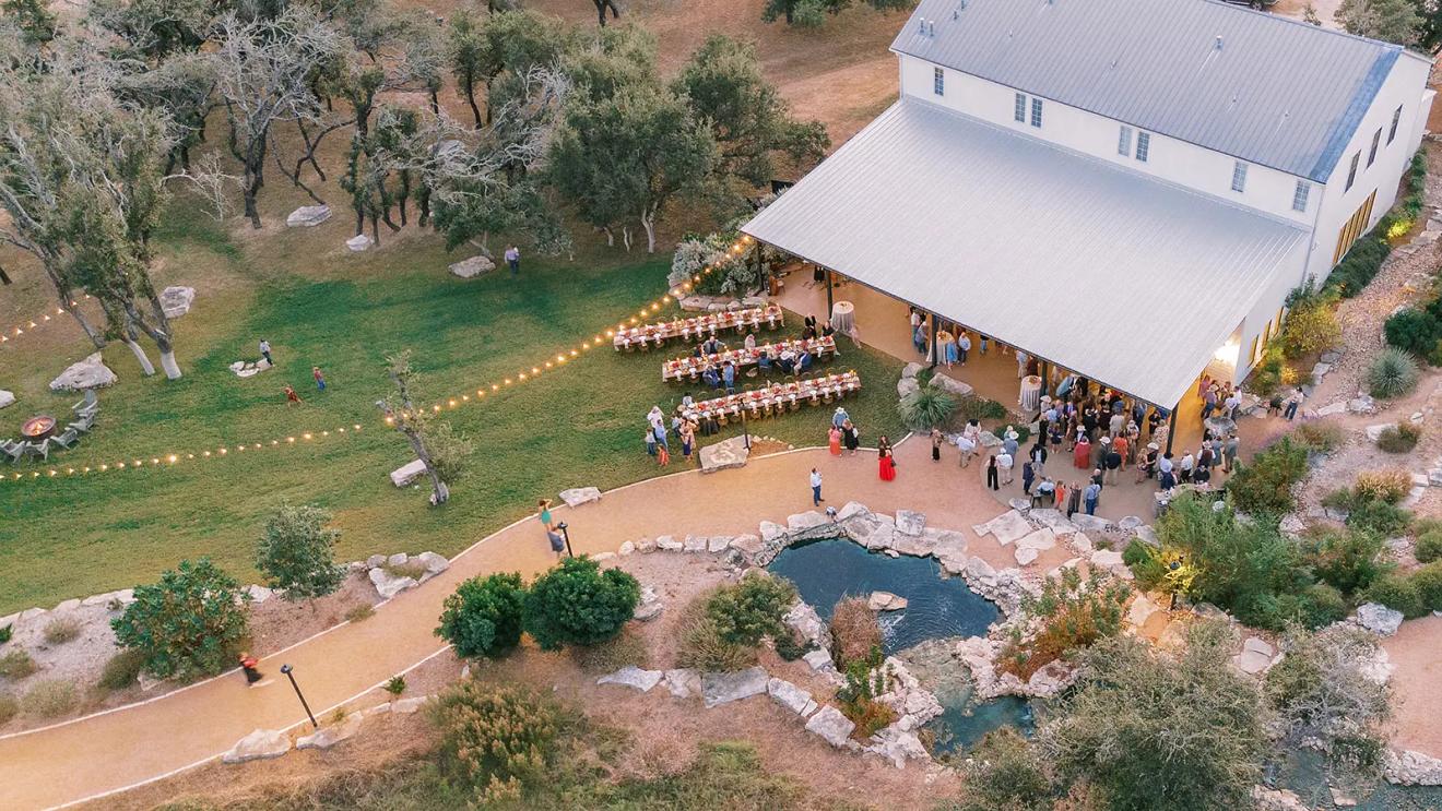 Aerial view of the Hall, its covered patio and string-lit dinner tables at Contigo Ranch, a Fredericksburg wedding venue