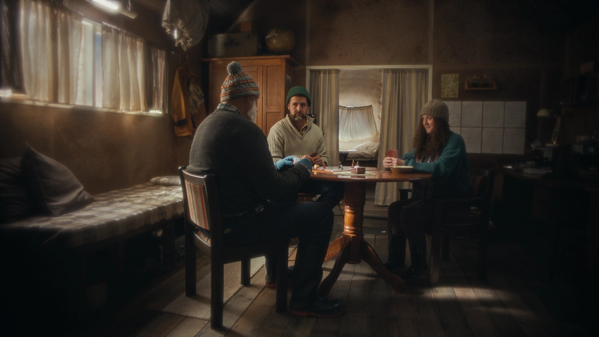 Four people sit around a table in a wood-panelled room in Yesterday Island.