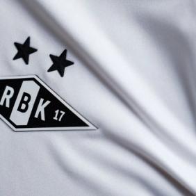 Nærbilde av Rosenborg BK-emblemet med to svarte stjerner brodert på en hvit fotballdrakt.