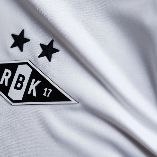 Nærbilde av Rosenborg BK-emblemet med to svarte stjerner brodert på en hvit fotballdrakt.