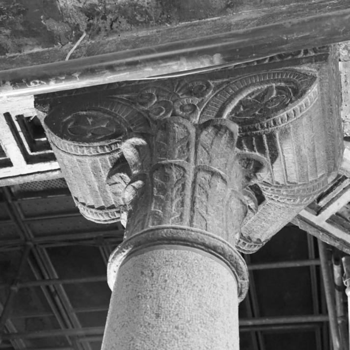 An ornate carved stone column capital with floral and scroll motifs supporting a coffered ceiling — by Nonspace