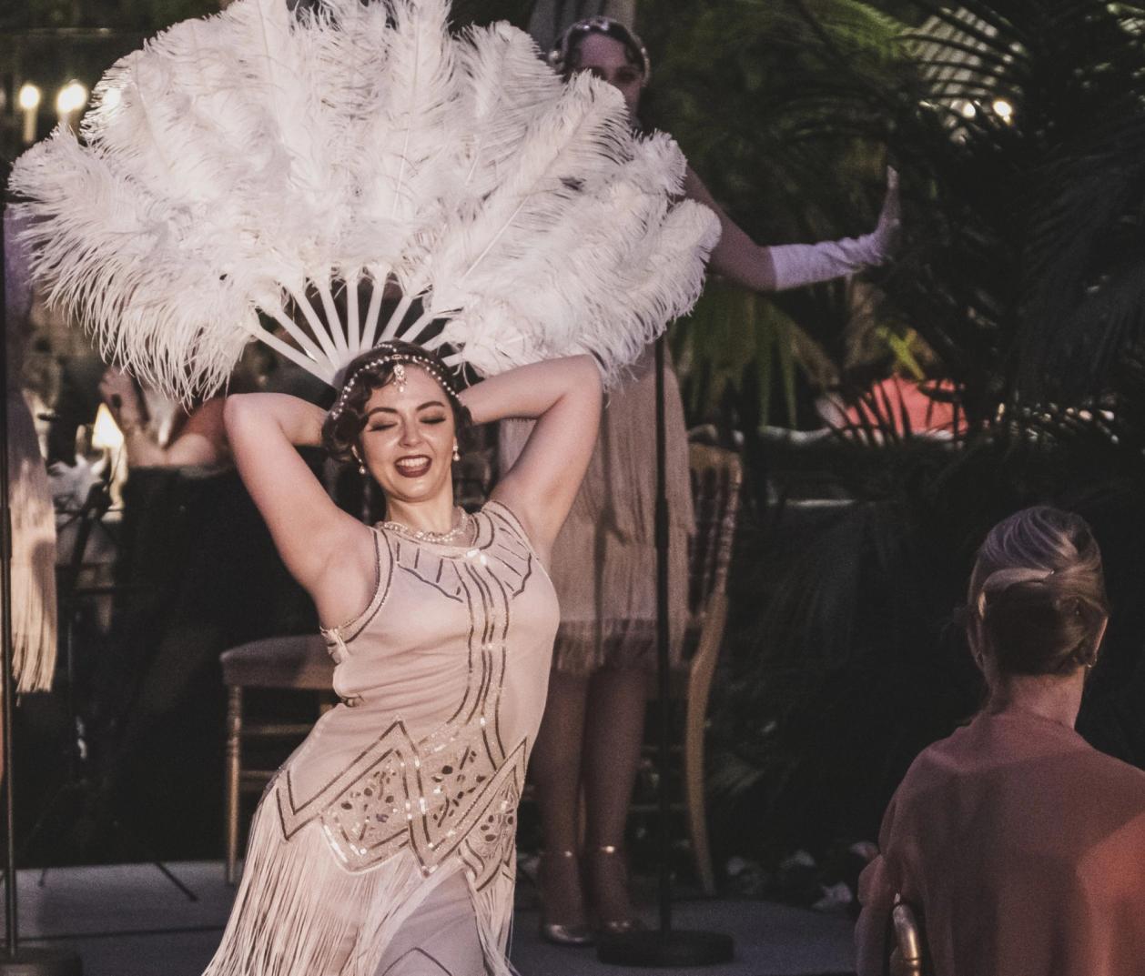 A performer in a 1920s flapper dress holds white feather fans above her head at a Gatsby-themed event — by Nonspace
