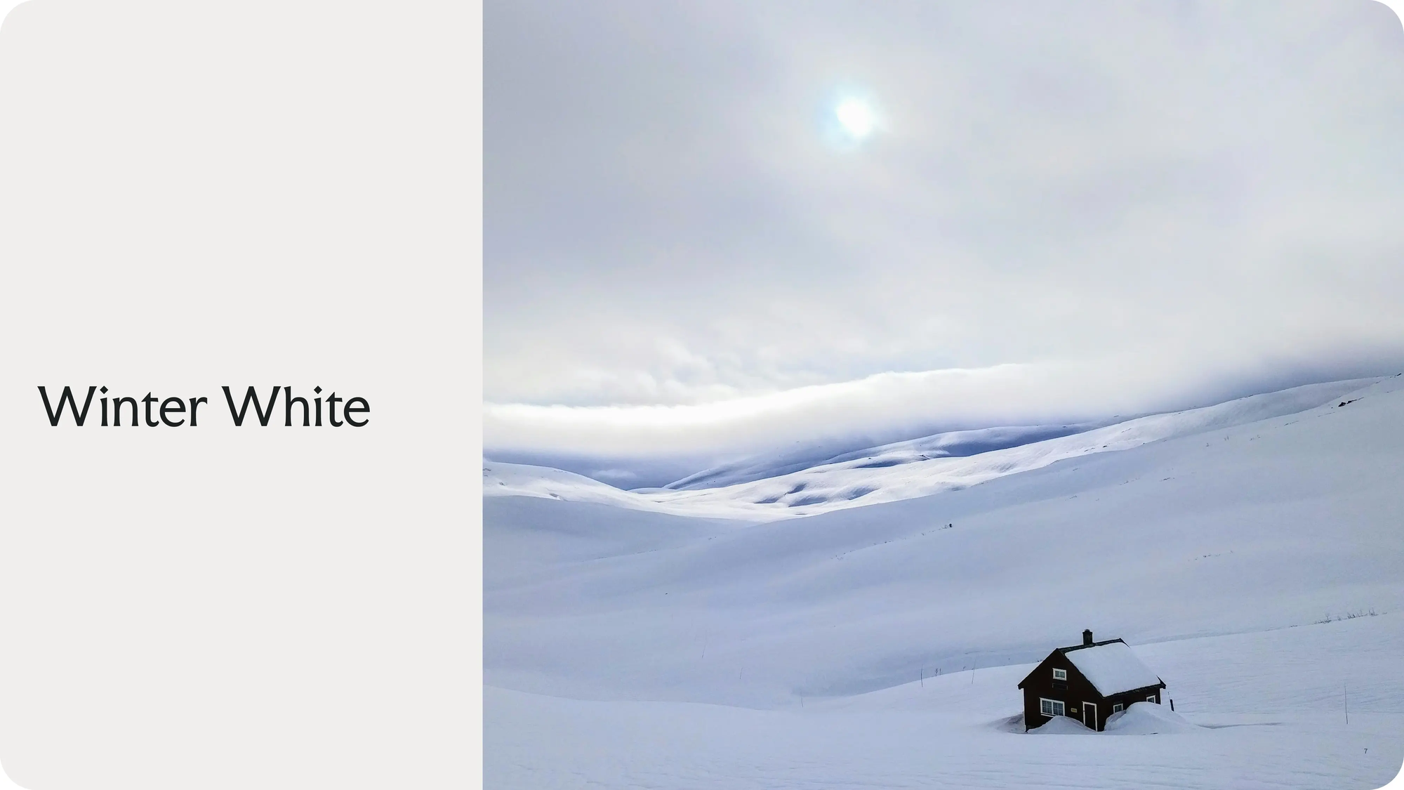 Et enslig mørkt trehus omgitt av snødekte fjell under en overskyet himmel med svak sol — av Nonspace