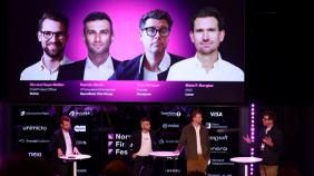 Four people on stage, audience in front, standing under large screen.