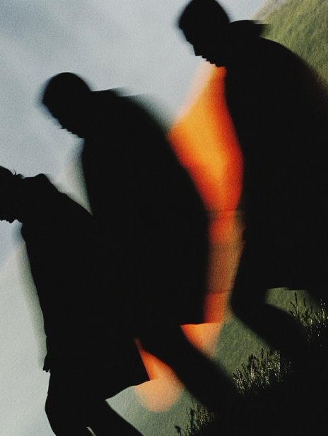 Blurry silhouettes of hikers walking uphill in low light, captured with motion blur, showcasing Yama outdoor apparel in a dramatic nature setting.