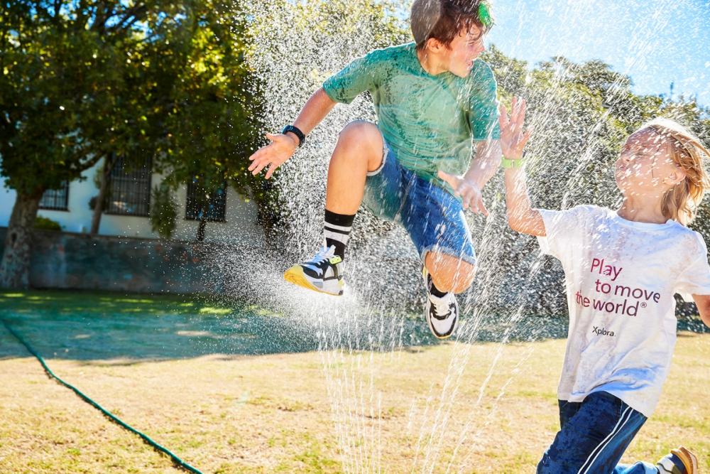 To barn leker i vannspruten fra en hagesprinkler på en solfylt gressplen — av Nonspace