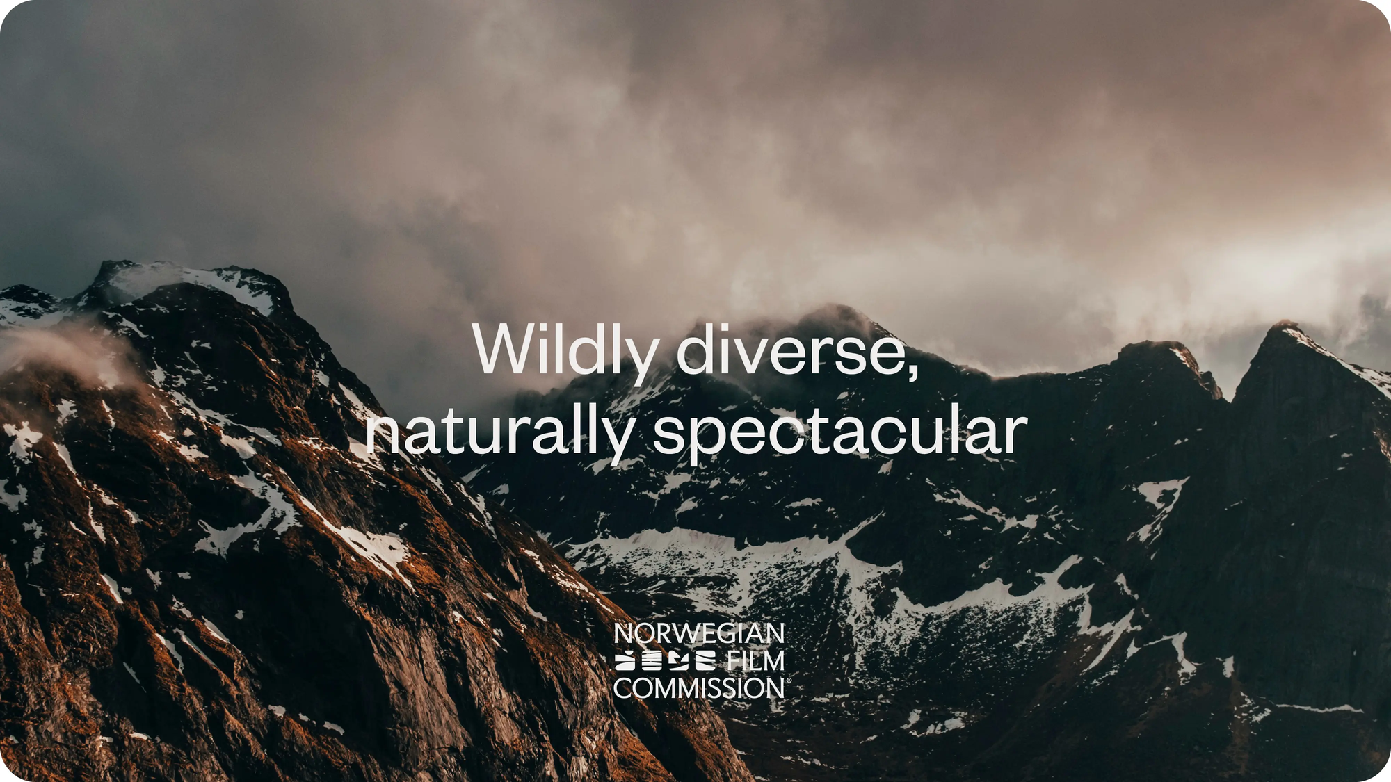 Snødekte fjelltopper under dramatisk skydekke med teksten Wildly diverse, naturally spectacular — av Nonspace