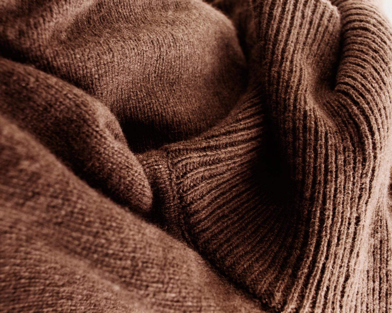 Close-up macro photograph of soft brown knitted fabric showing detailed texture and ribbed pattern.