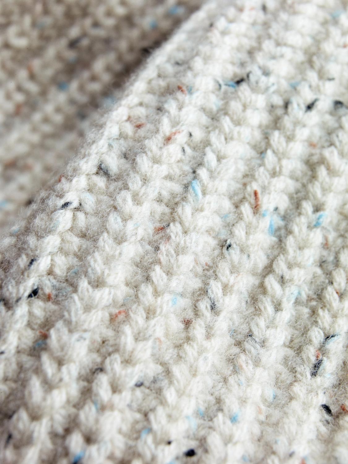 Close-up texture of a soft, cream-colored knitted wool fabric with speckled yarn details.