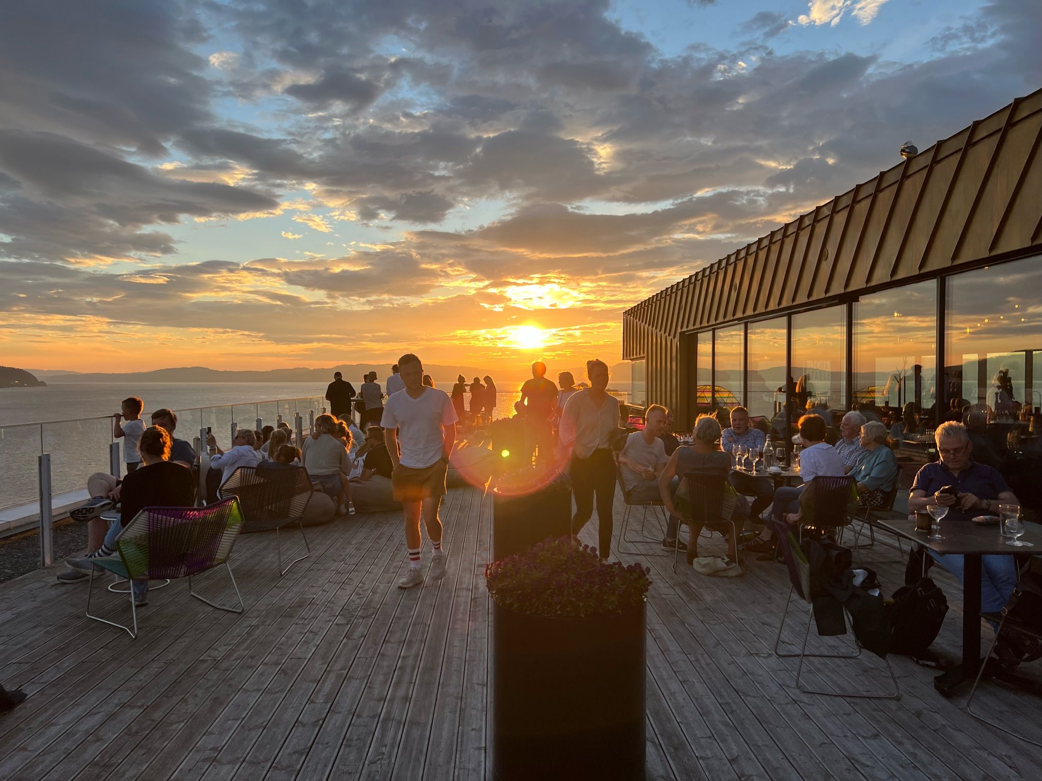 People enjoying a sunset on the rooftop terrace of Clarion Hotel Trondheim, overlooking the water with a dramatic sky and warm evening light.