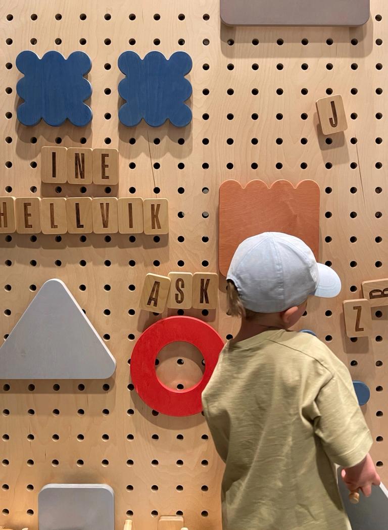 Child interacting with a wooden pegboard wall at Kunstsilo Kids exhibit, arranging colorful geometric shapes and letter blocks in an interactive play installation.