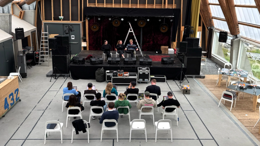 The Nonspace team gathered at Stokkøya, sitting in a hall facing a small stage during a workshop presentation.