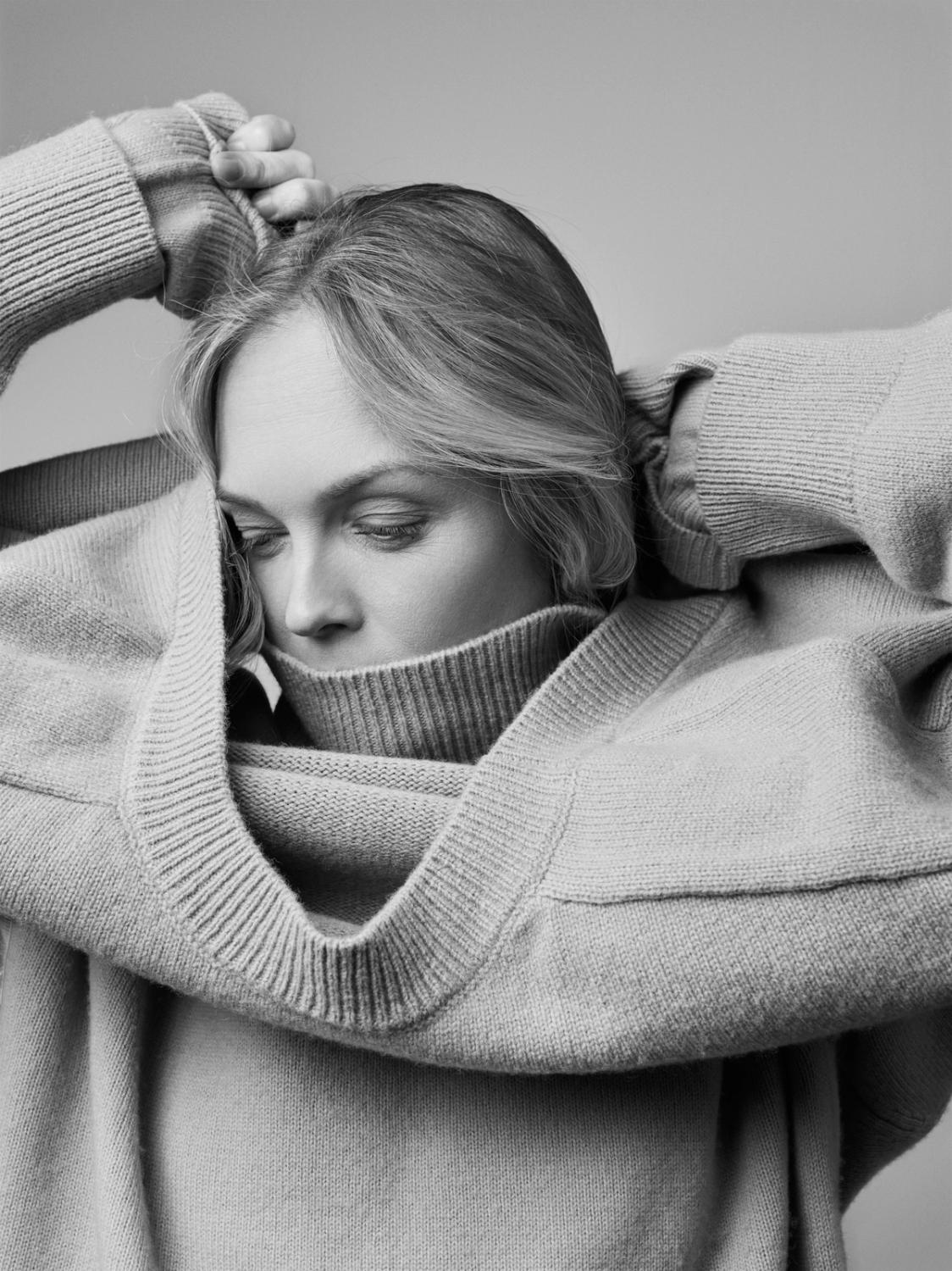 Woman putting on a soft knitted sweater, close-up black-and-white portrait showcasing Plateau’s timeless knitwear.