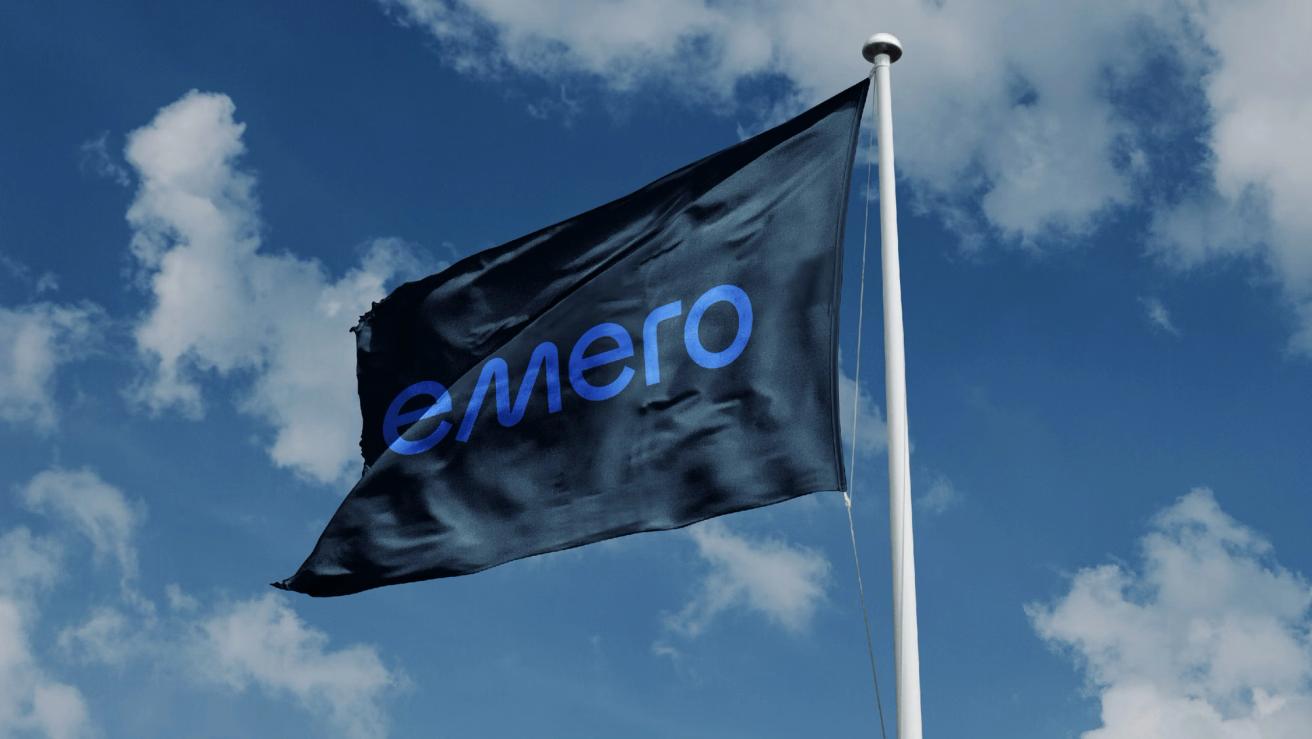 A black flag with the blue "emero" logo waving against a cloudy blue sky — by Nonspace
